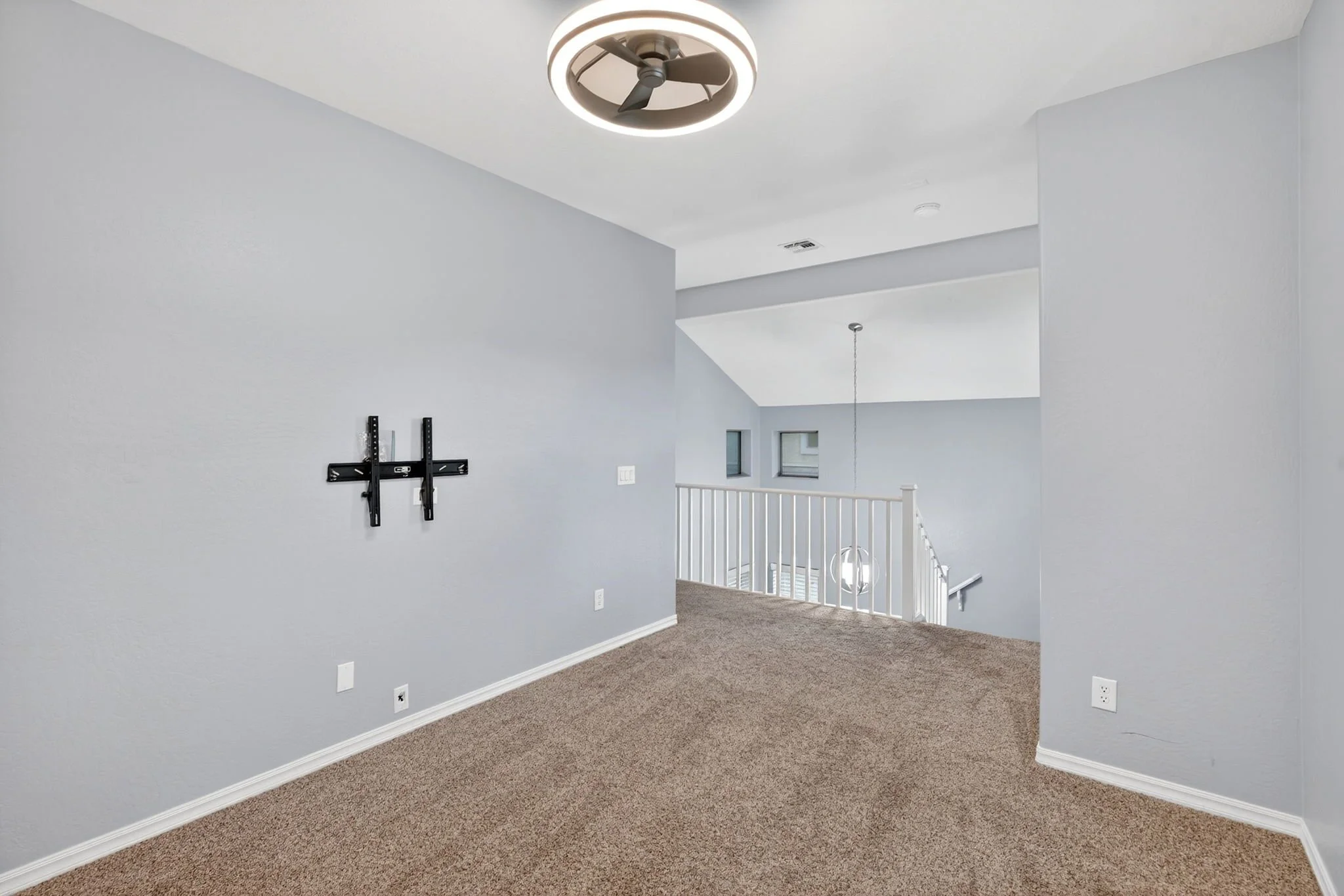 Modern interior space with light gray walls, a ceiling fan with light, a staircase with white railing, small windows, and a mounted wall bracket.