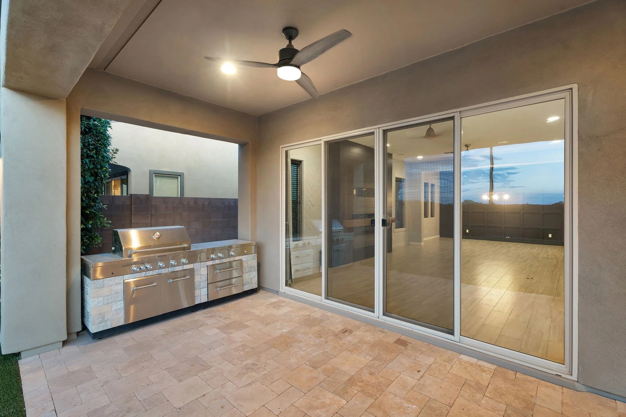 Outdoor patio area with built-in stainless steel grill, beige tiled flooring, sliding glass door, ceiling fan, and a view of the backyard