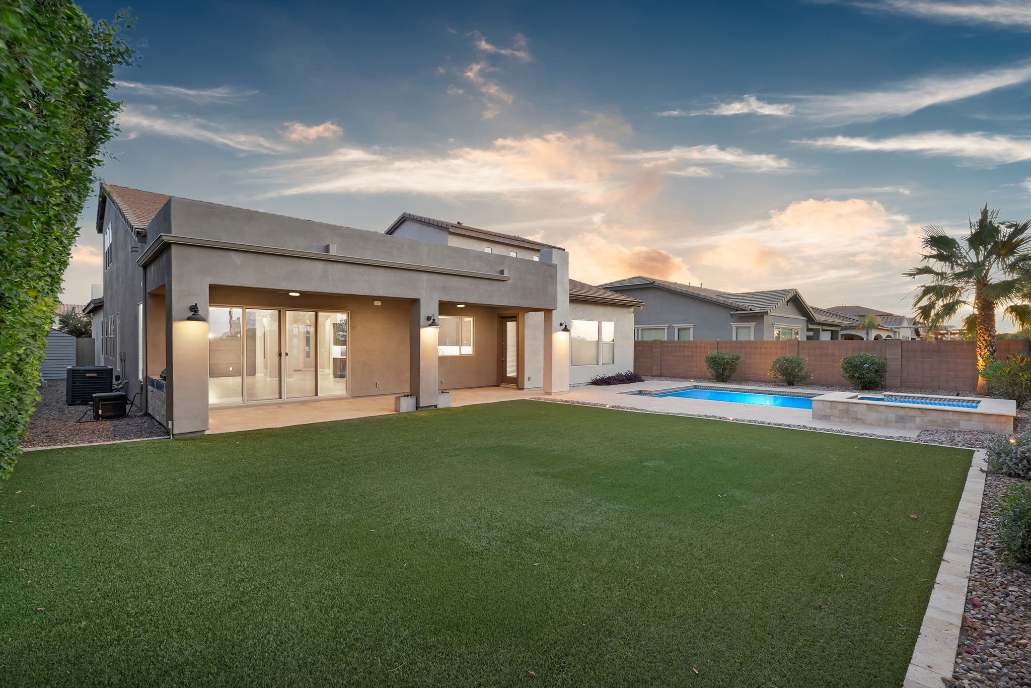 Modern two-story house with a backyard, green lawn, swimming pool, and patio area during sunset.