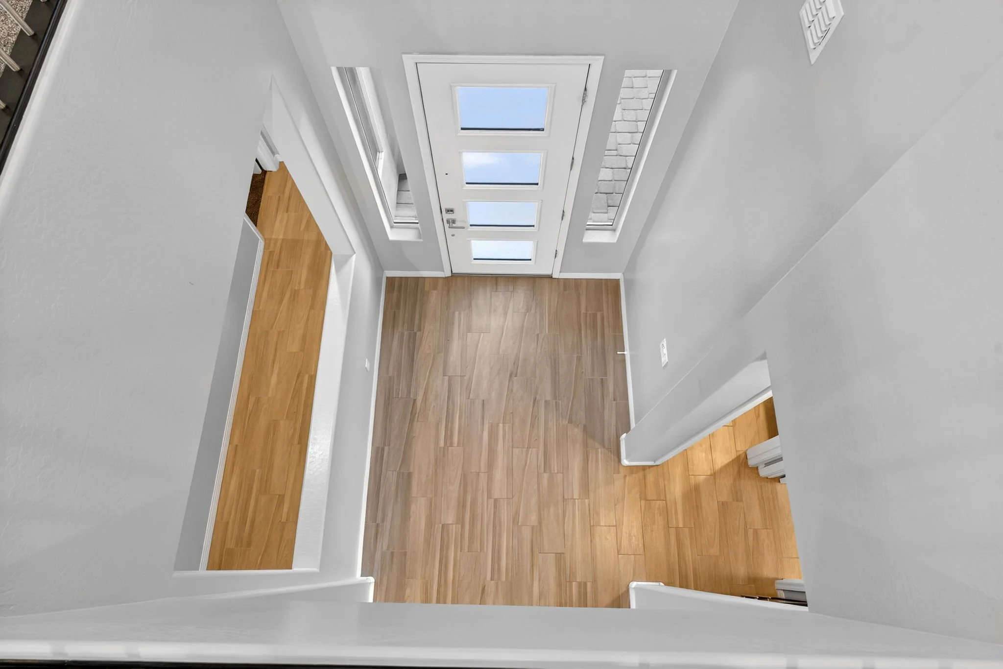 Empty interior space with white walls, wood flooring, and a door with glass panels leading outside, seen from a high angle.