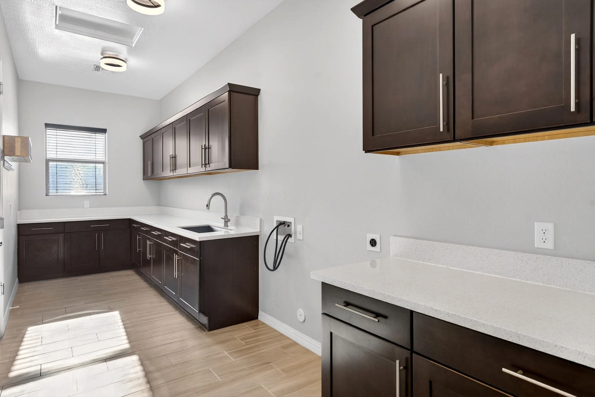 Modern kitchen with dark brown cabinets, white countertops, a window, and wood-like flooring.