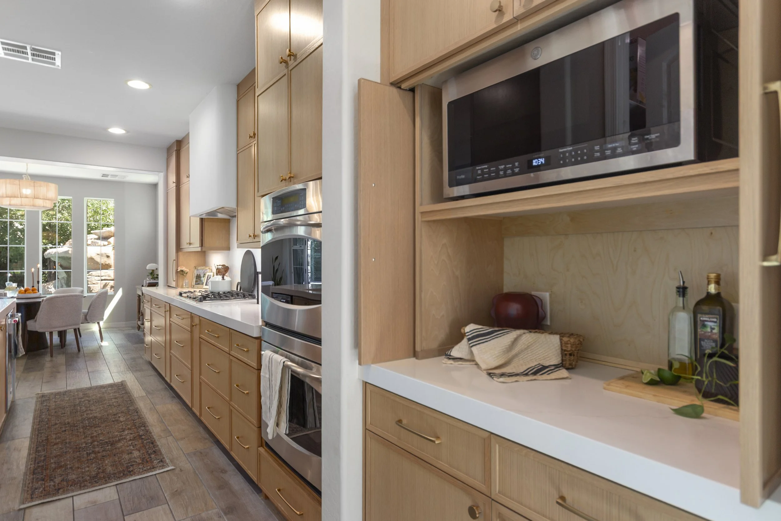 Kitchen with wooden cabinets, stainless steel oven and microwave, white countertop, and open shelving with decorative items.