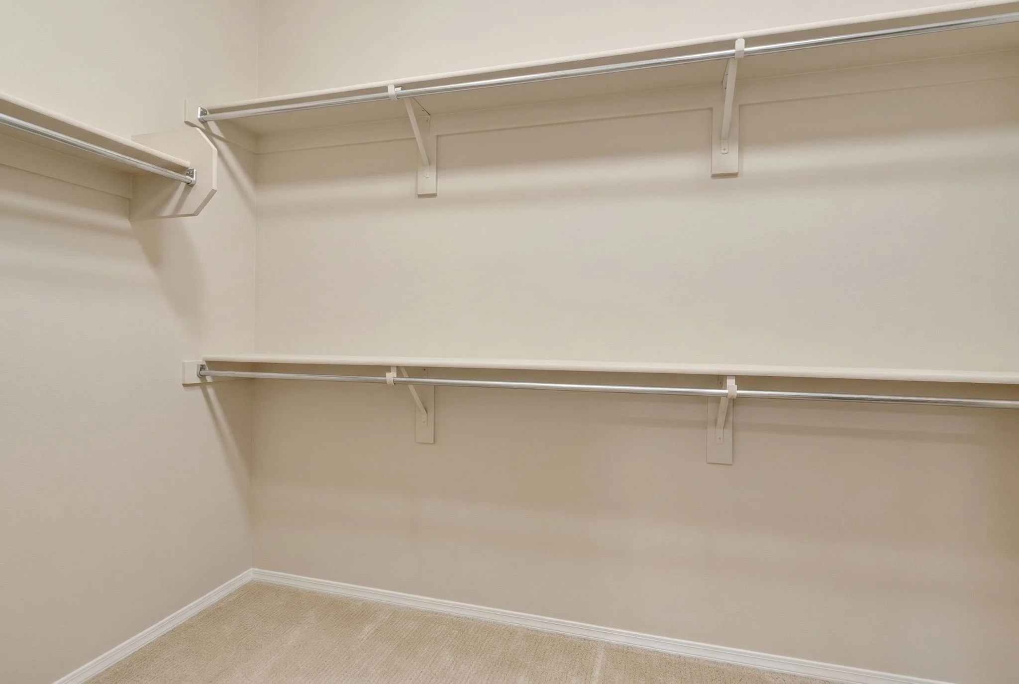 Empty walk-in closet with white wire hanging rods and shelves, beige carpet, and plain walls.
