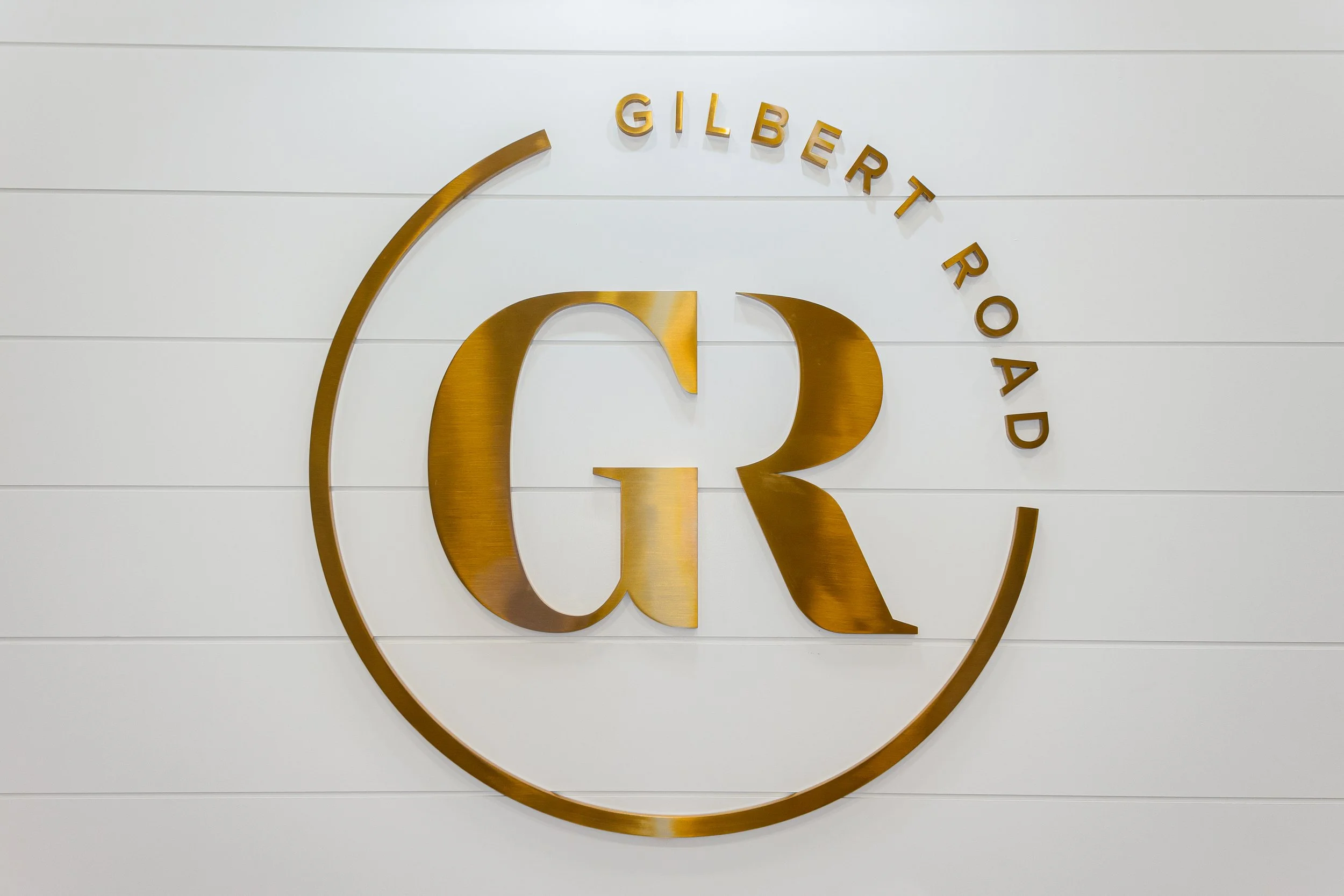 Golden logo of Gilbert Road on a white wall with horizontal panels.