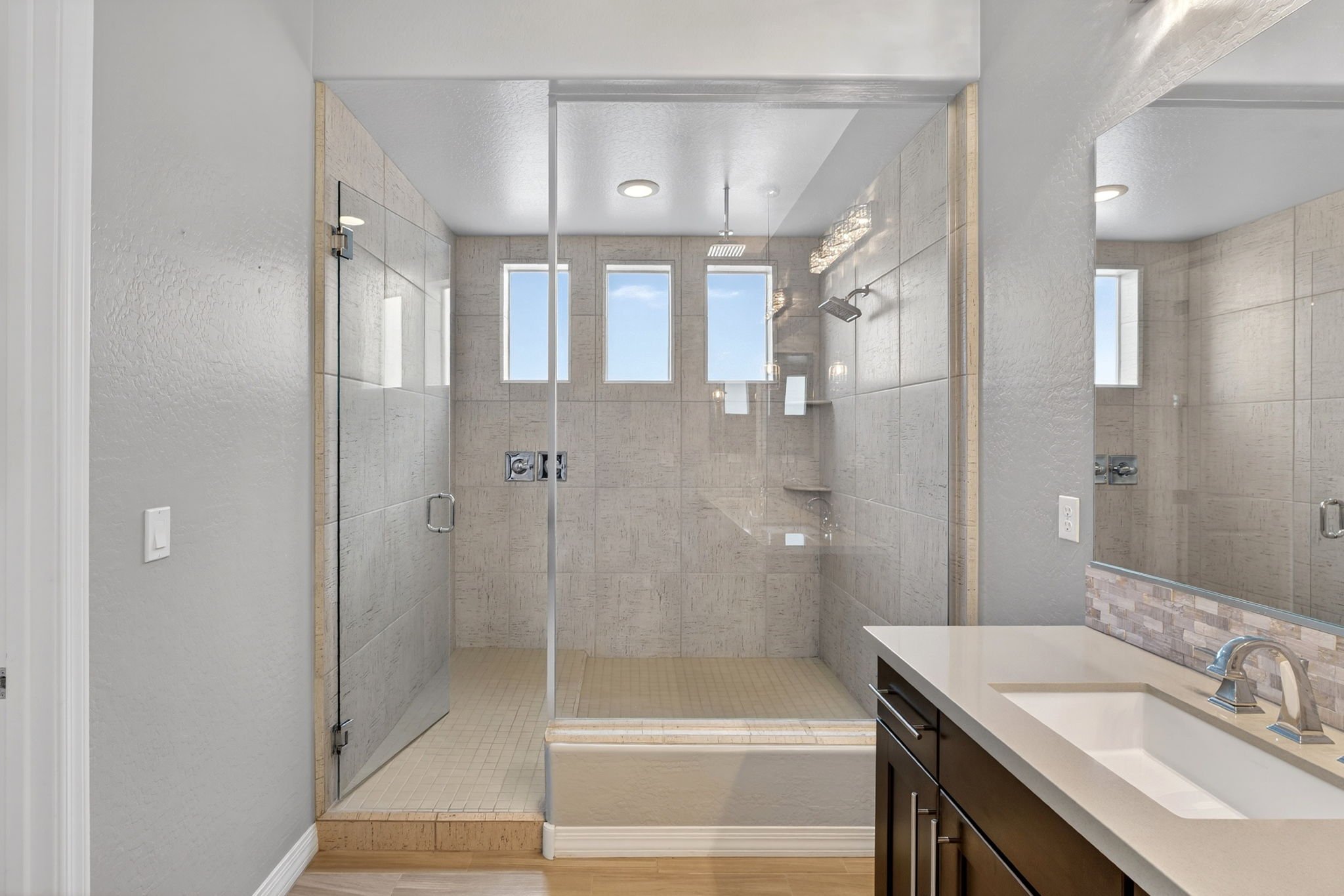 Modern bathroom with a frameless glass shower enclosure, beige tile walls, skylight windows, white ceiling, and a dark wood vanity with a white countertop and sink.