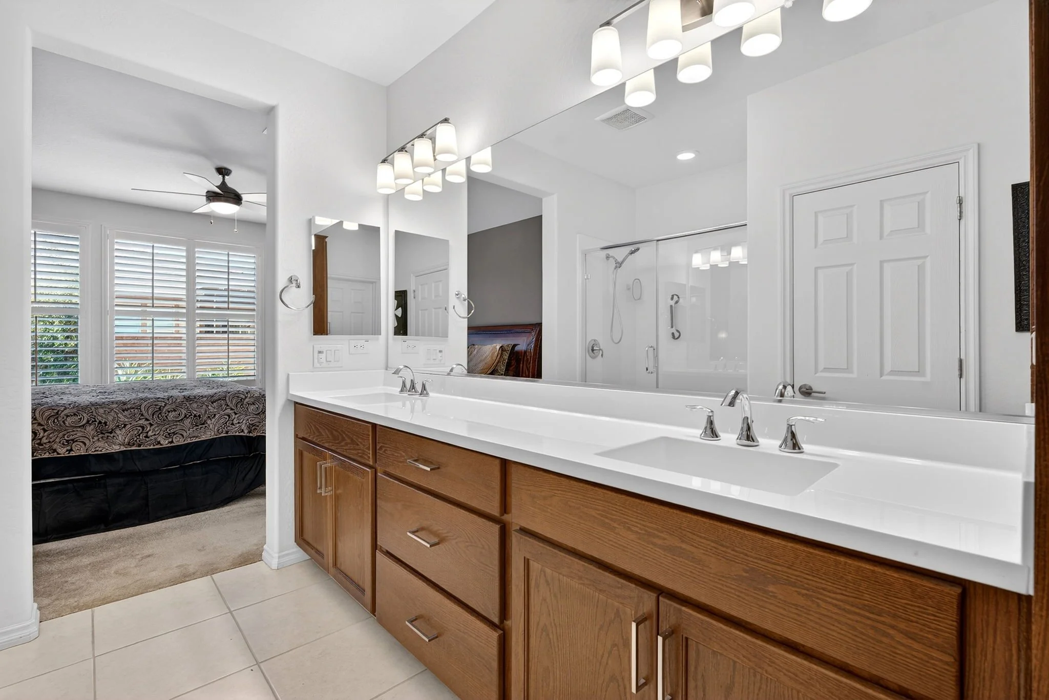 Bathroom with double sink vanity, large mirror, shelves, and a shower area with glass door.