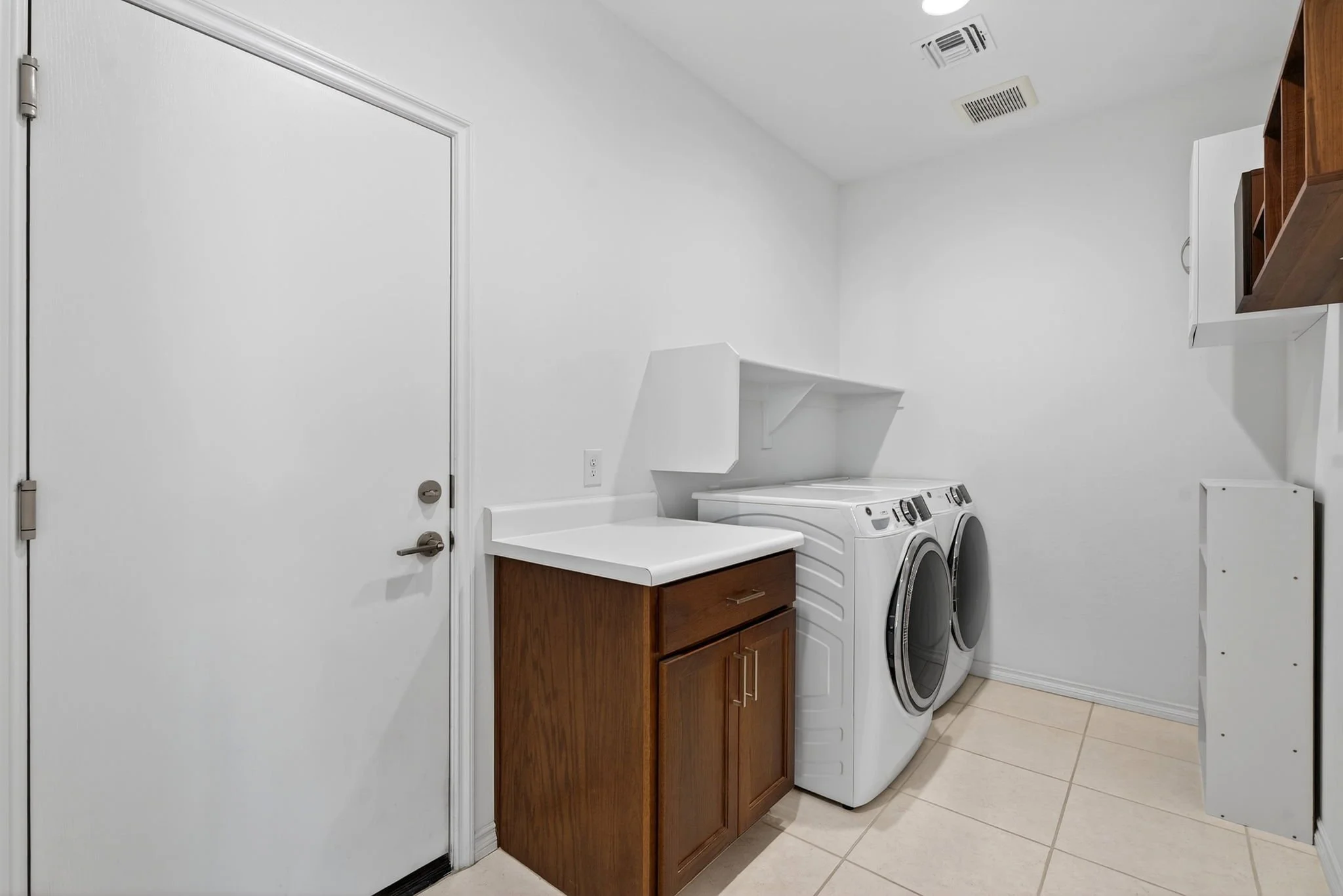 Laundry room with white walls, a white washing machine and dryer, a wooden cabinet, and a white countertop.