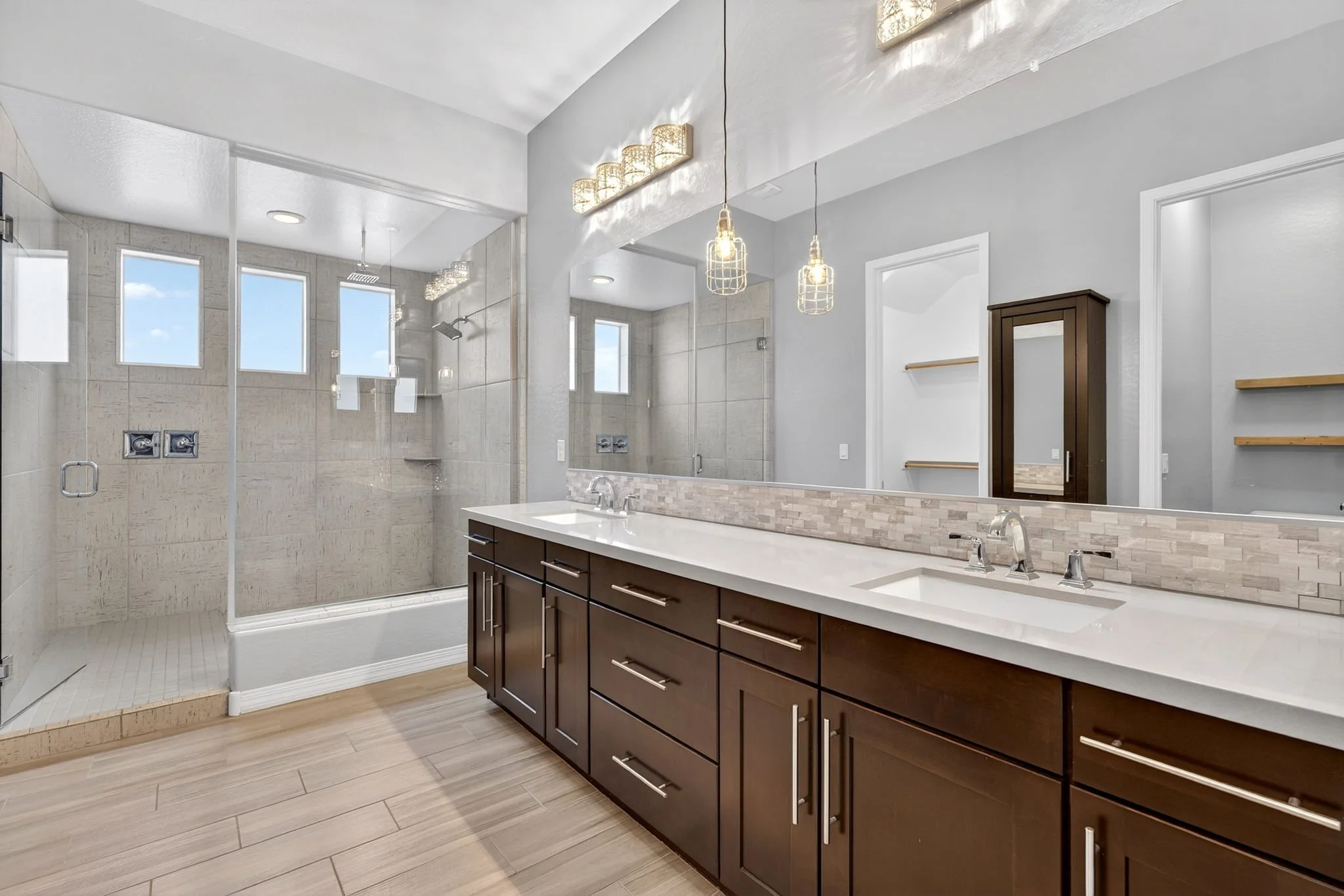 Modern bathroom with a glass-enclosed shower, double sink vanity with dark wood cabinets, a large mirror, and decorative pendant lighting.