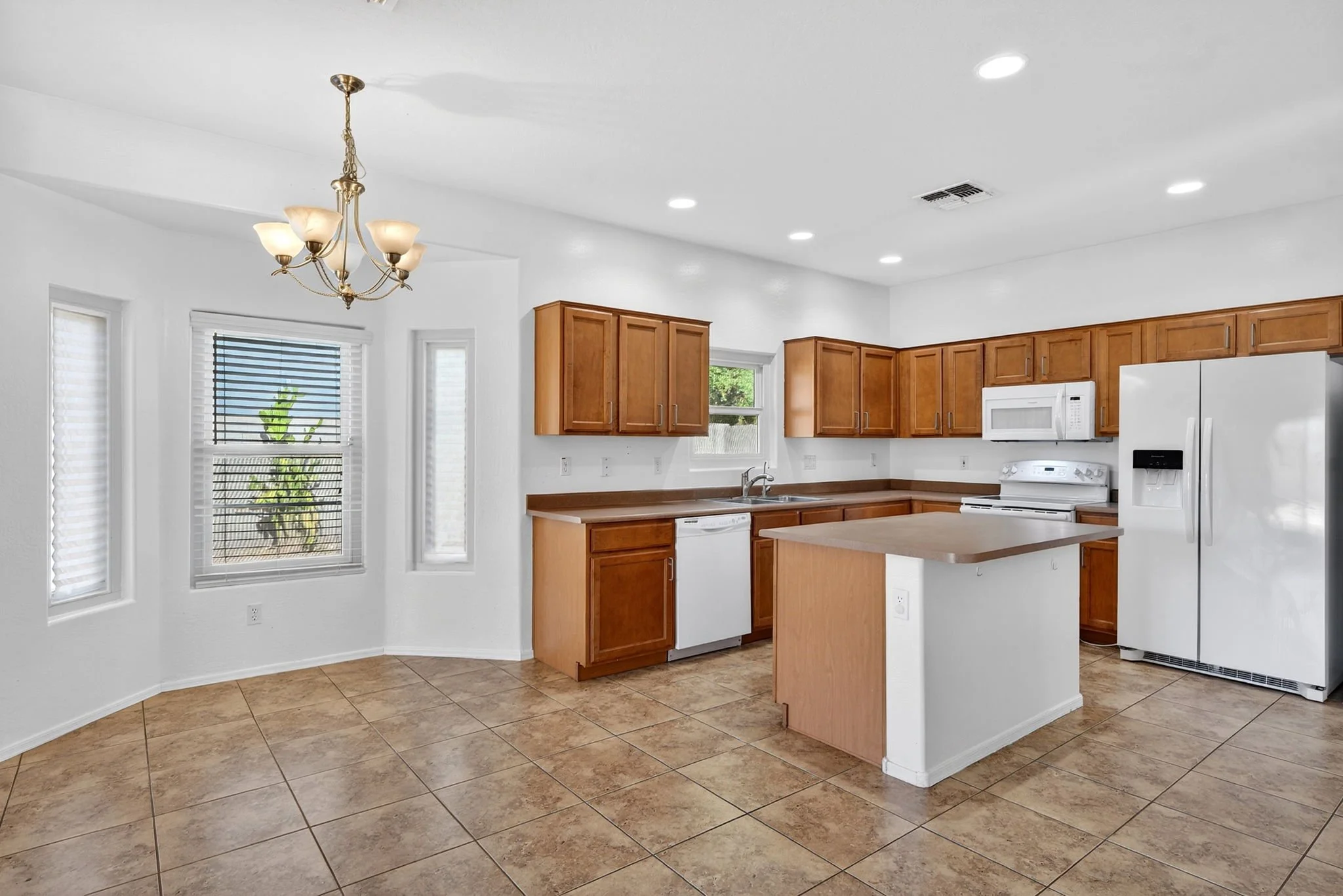 Bright kitchen with wooden cabinets, white appliances, tiled floor, multiple windows, and a chandelier.
