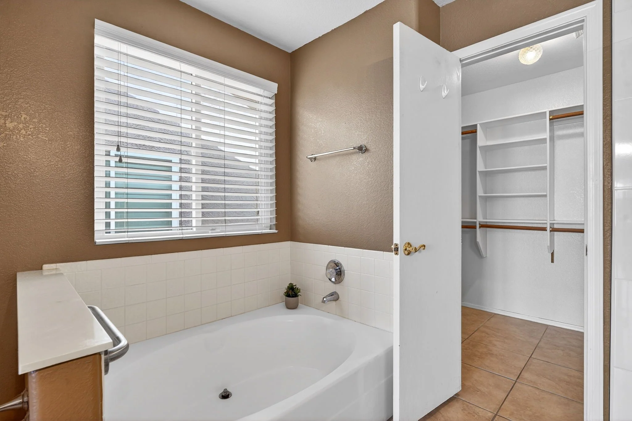 Bathroom with a bathtub, window with blinds, and an open closet with shelves and hanging space.