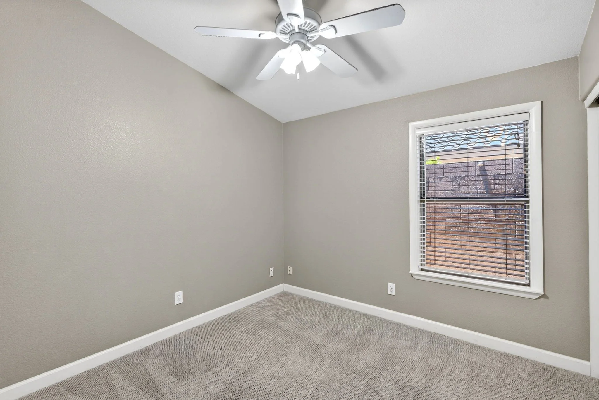 Empty room with beige walls, white baseboards, a window with blinds, and a ceiling fan with lights.