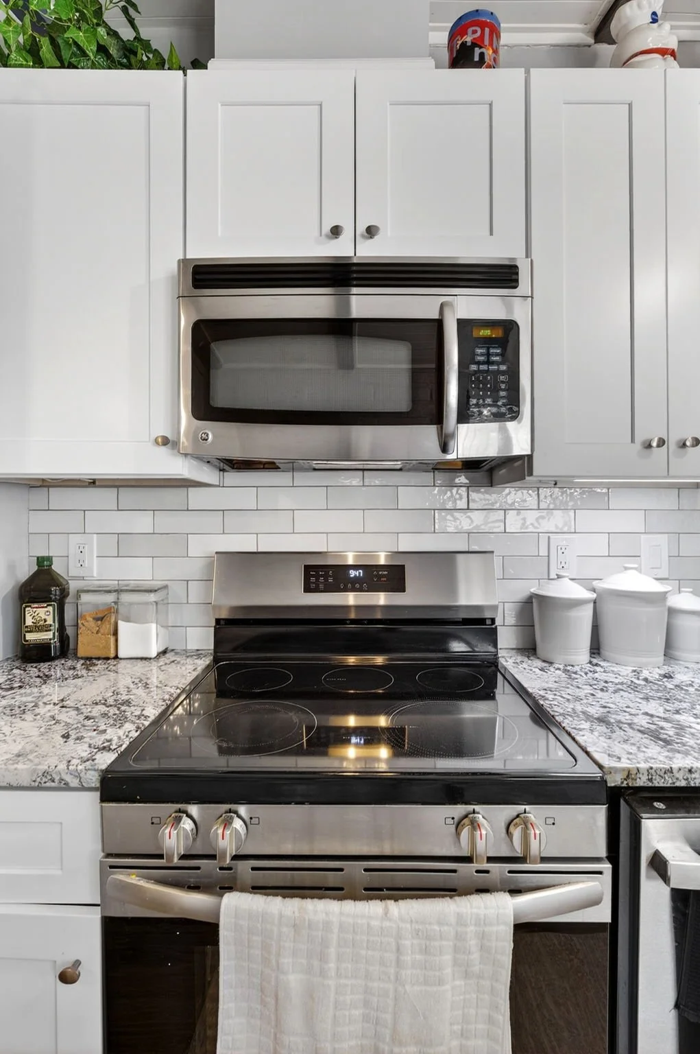Modern kitchen with white cabinets, stainless steel microwave and oven, granite countertops, and a white tiled backsplash.