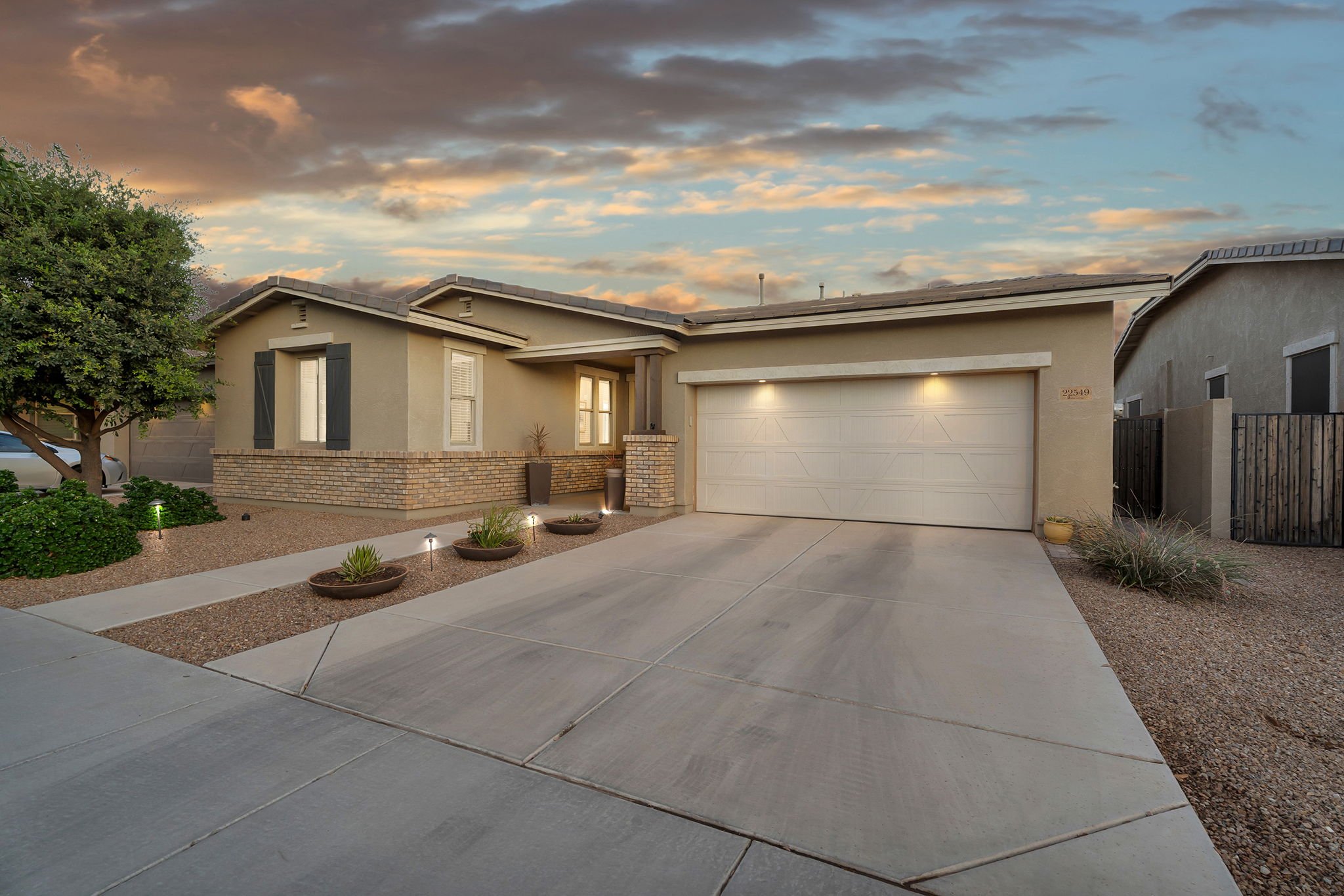 Front exterior view of a modern suburban house with a landscaped yard and a driveway during sunset.