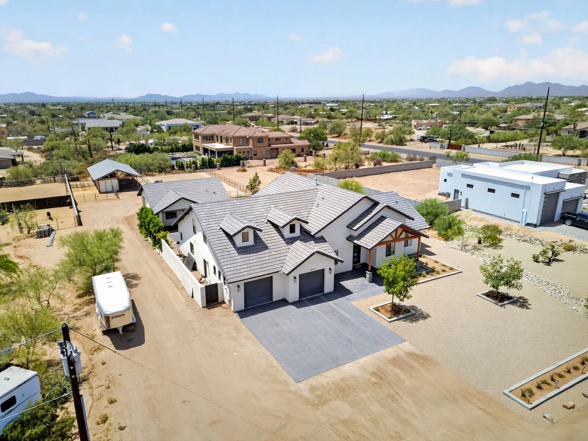 An aerial view of a residential neighborhood with new houses, some under construction, in a semi-arid landscape with distant mountains in the background.