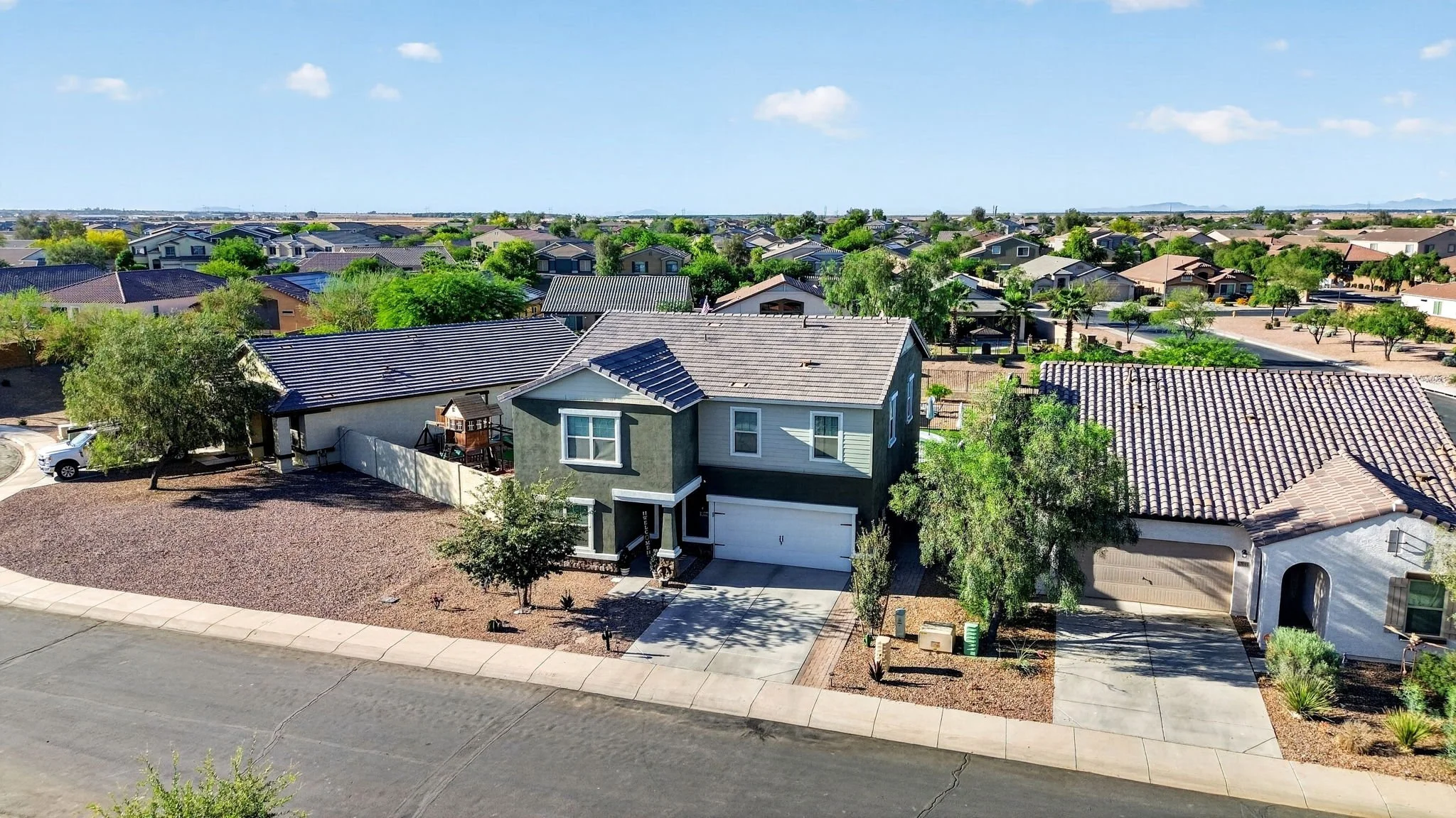 Aerial view of a suburban neighborhood with various houses, trees, and a clear blue sky.