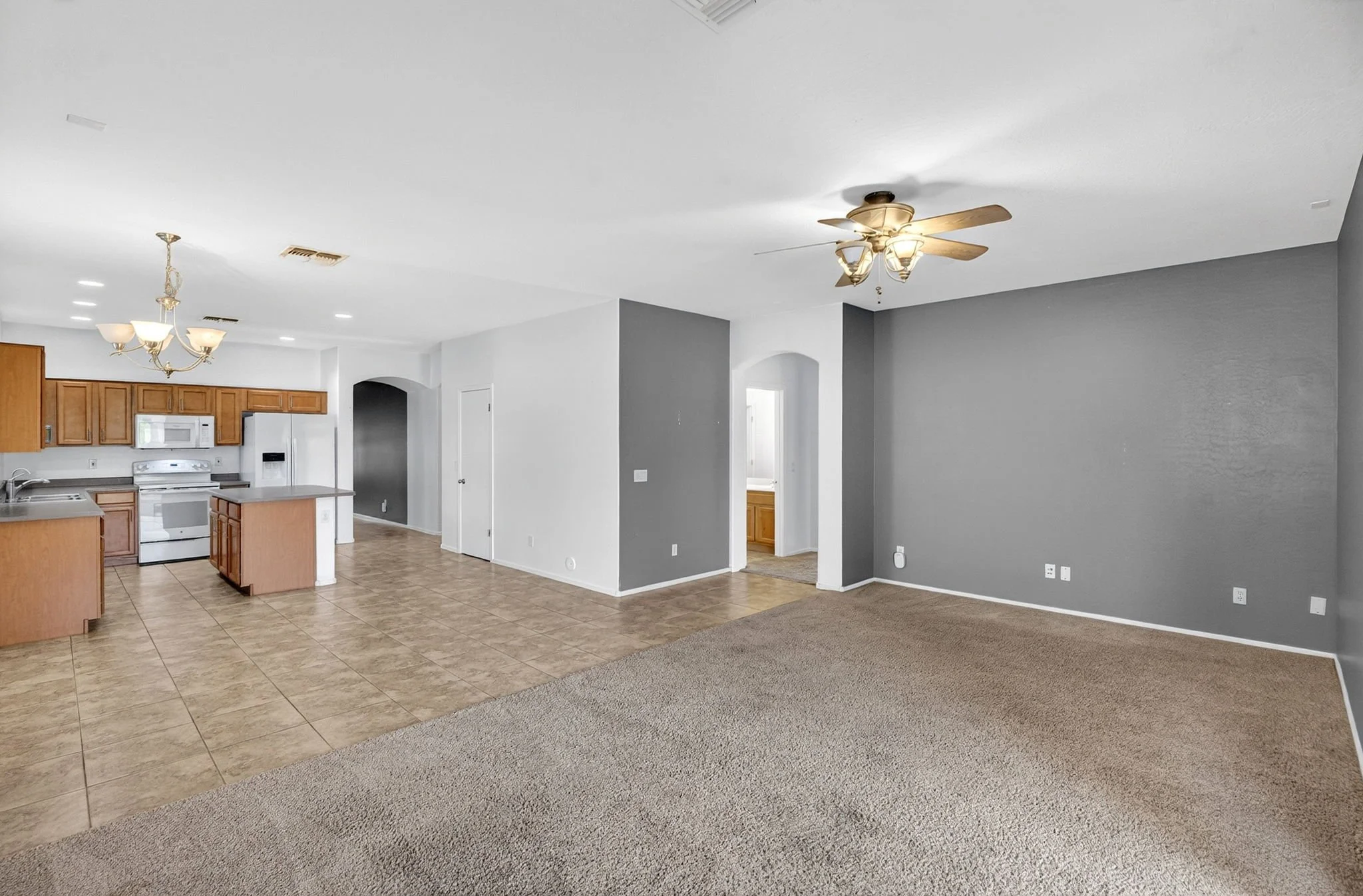 Open-concept living space with a kitchen and dining area, vinyl and carpet flooring, ceiling fans, and neutral-colored walls.
