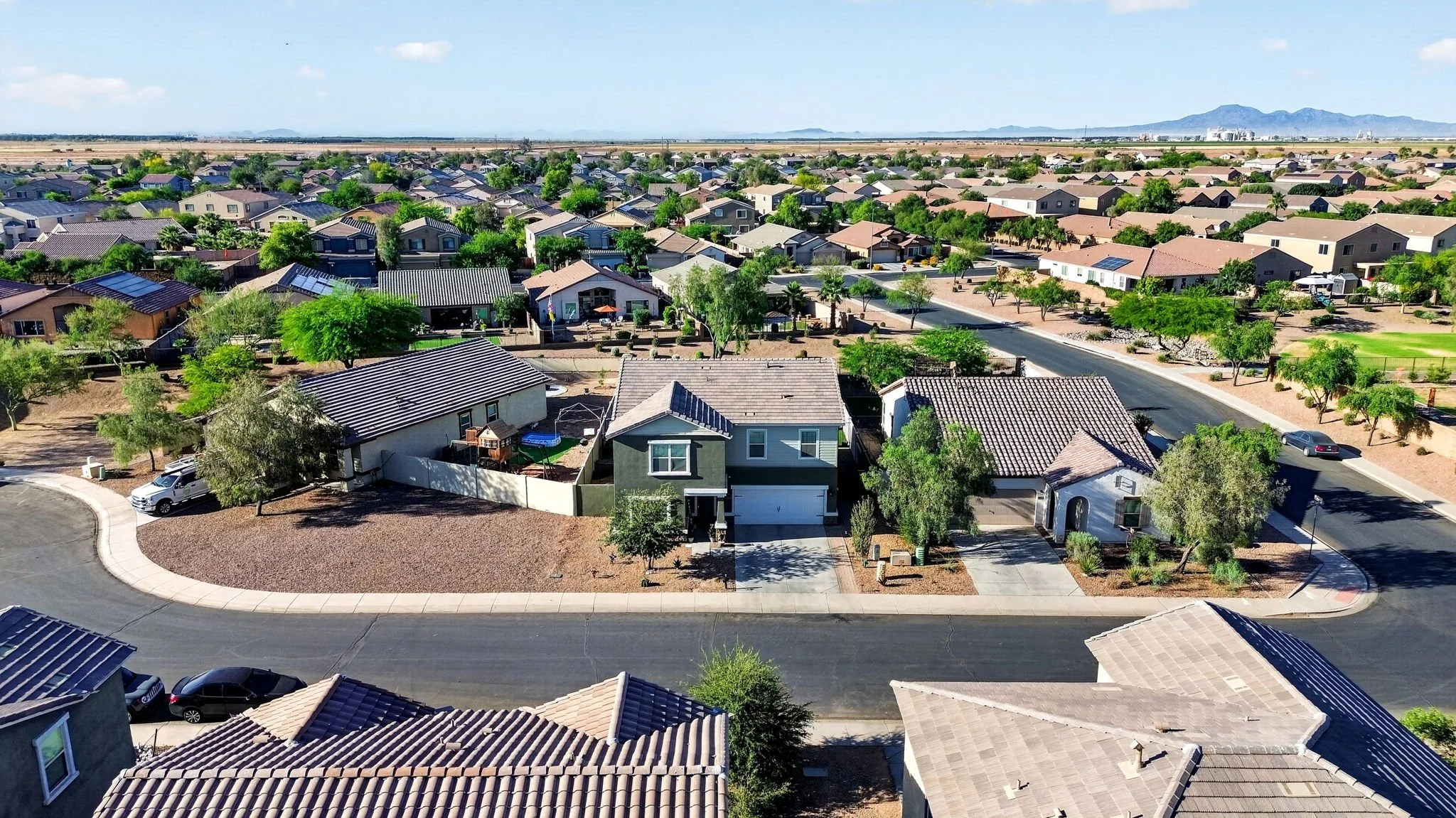 Aerial view of a suburban neighborhood with houses, trees, and streets, with mountains in the background under a clear blue sky.