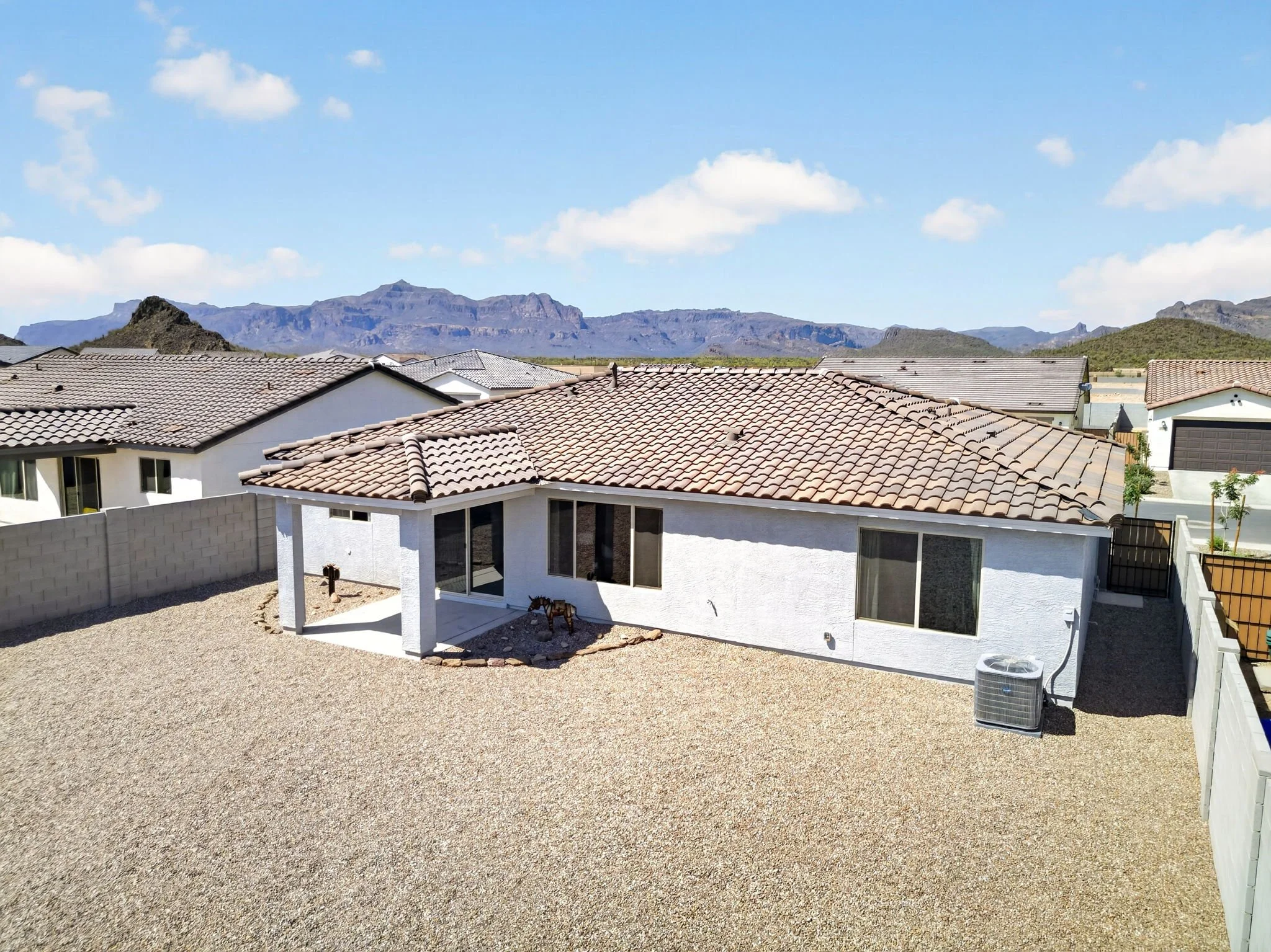View of rooftops of residential houses with mountains in the background under a blue sky with scattered clouds.