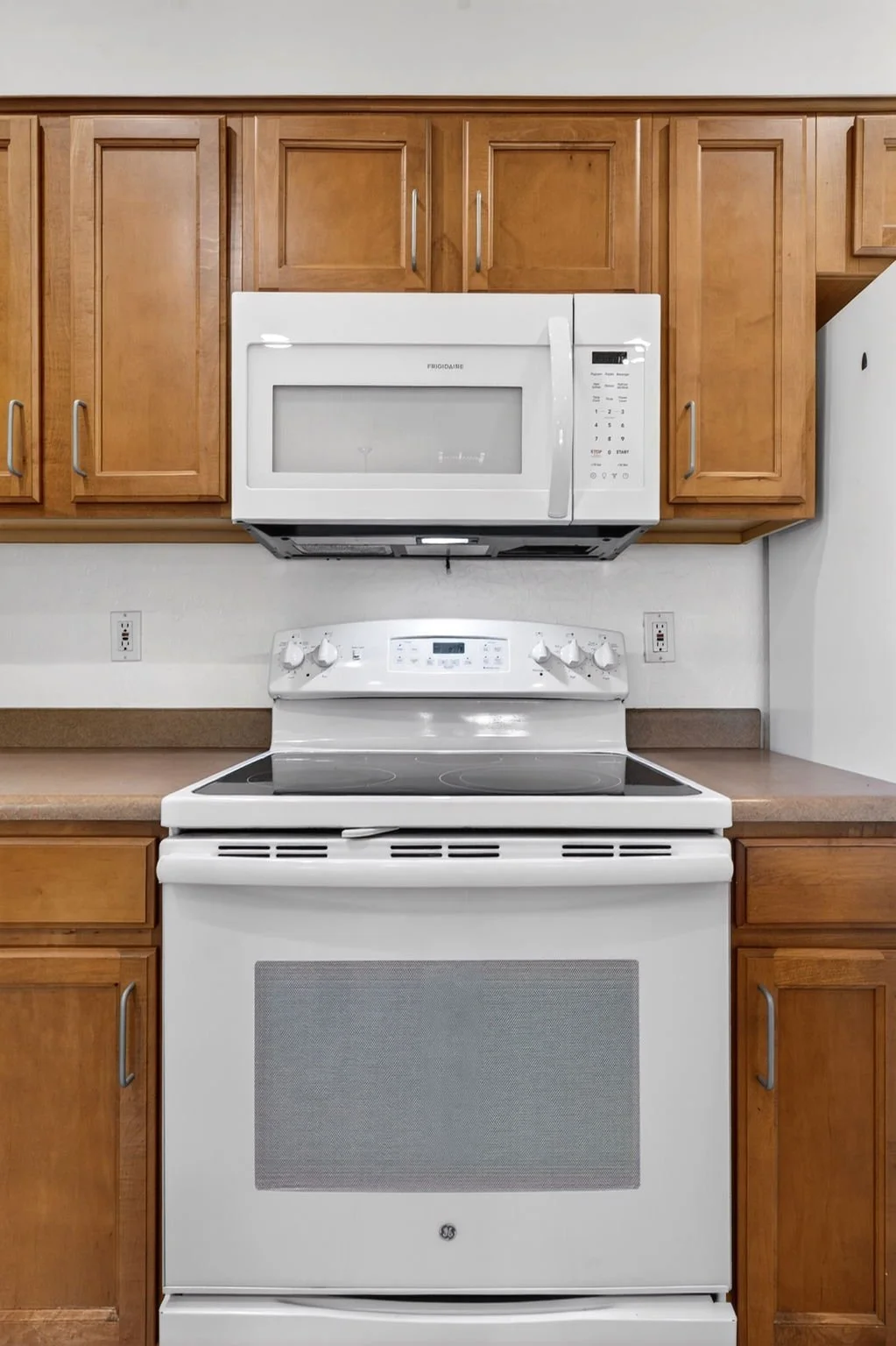 Kitchen with white stove and microwave, wooden cabinets, and beige countertops.