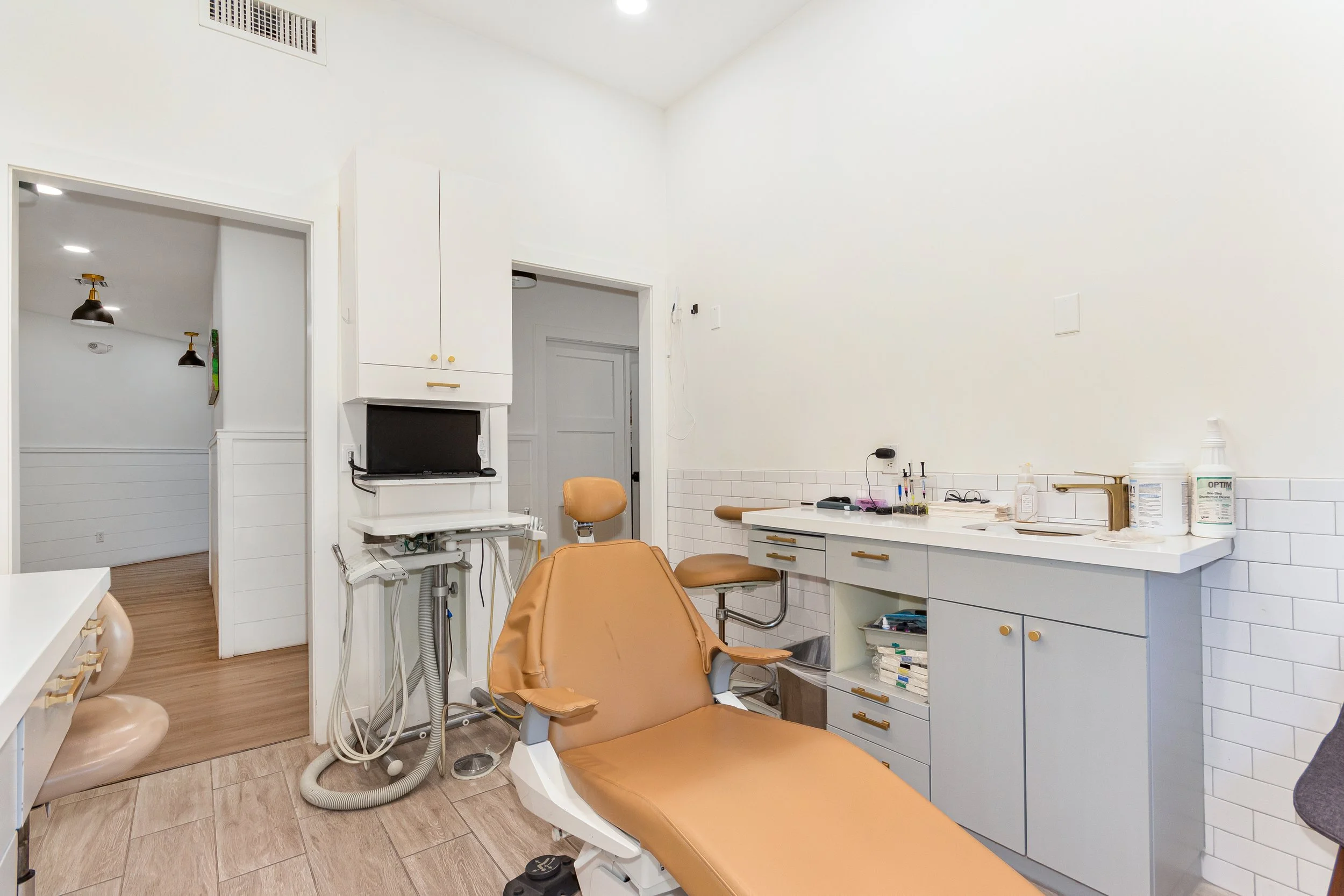 A clean dental examination room with a dental chair, medical equipment, and cabinets.