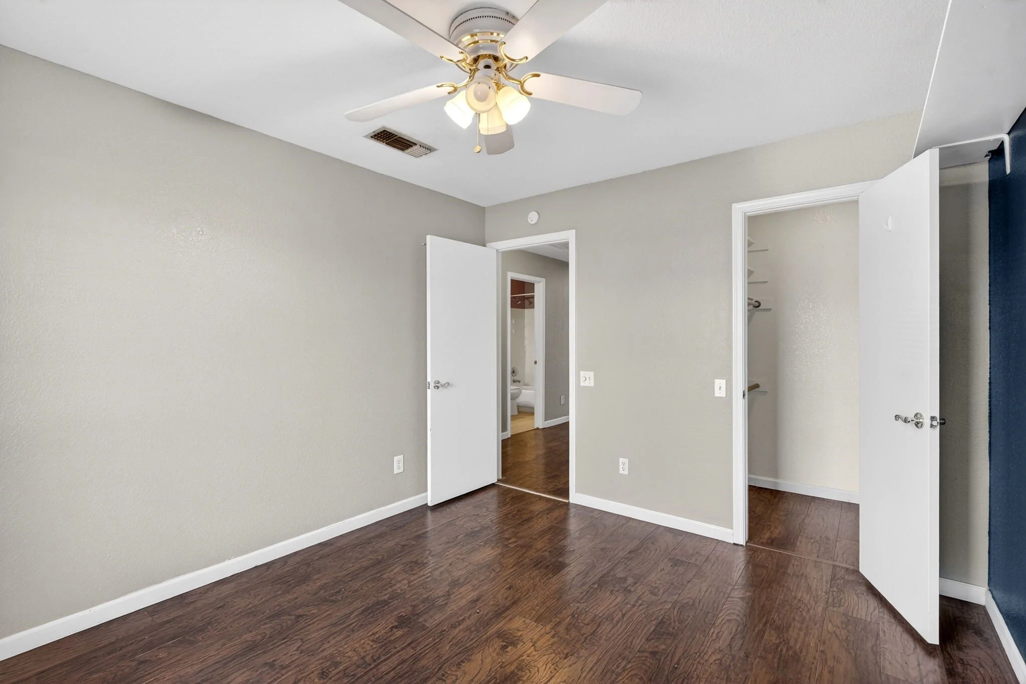 Empty room with hardwood floors, beige walls, a ceiling fan with lights, and open closet doors.