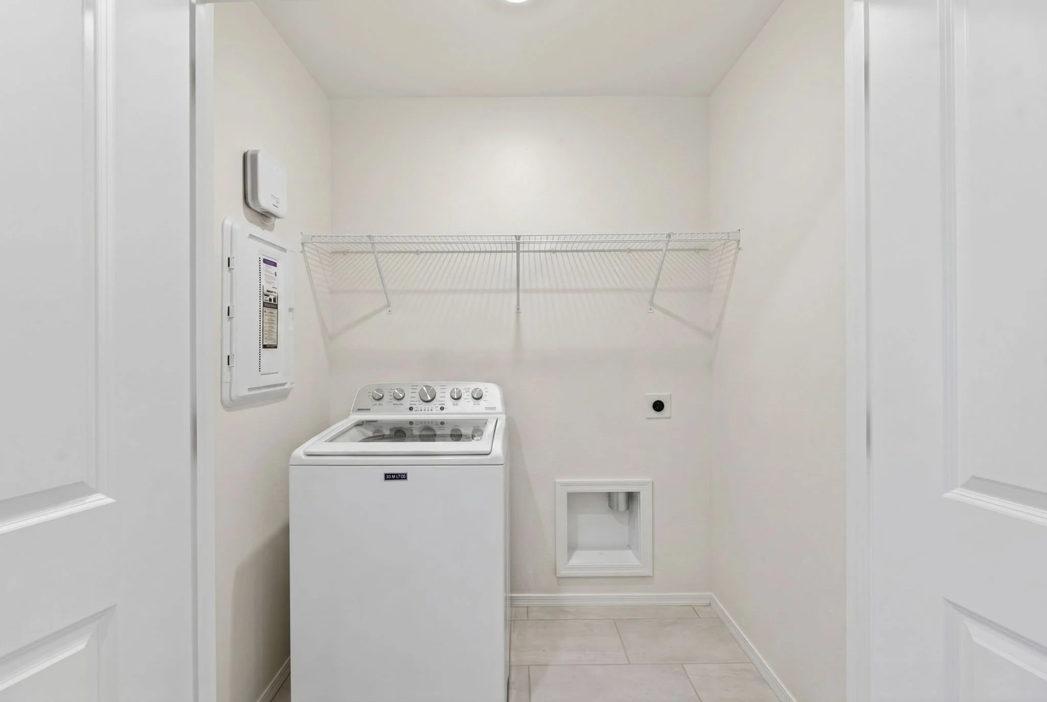 Empty laundry room with a top-loading washing machine, a wire shelf above, and a small vent near the floor.