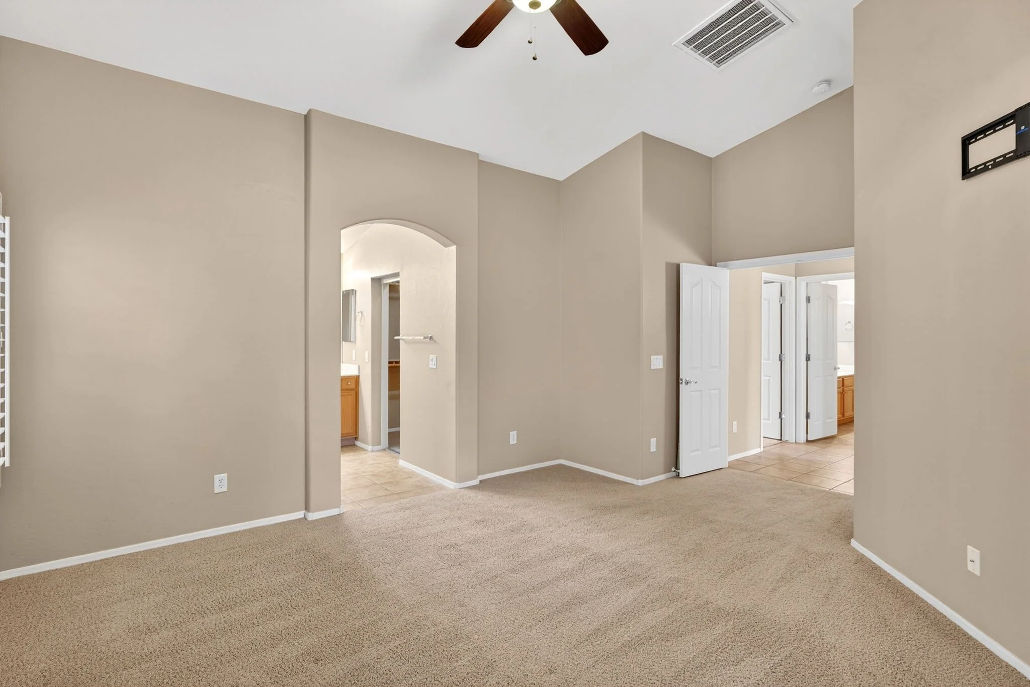 Interior of a house with beige walls, beige carpet, white doors, and a ceiling fan with wooden blades.