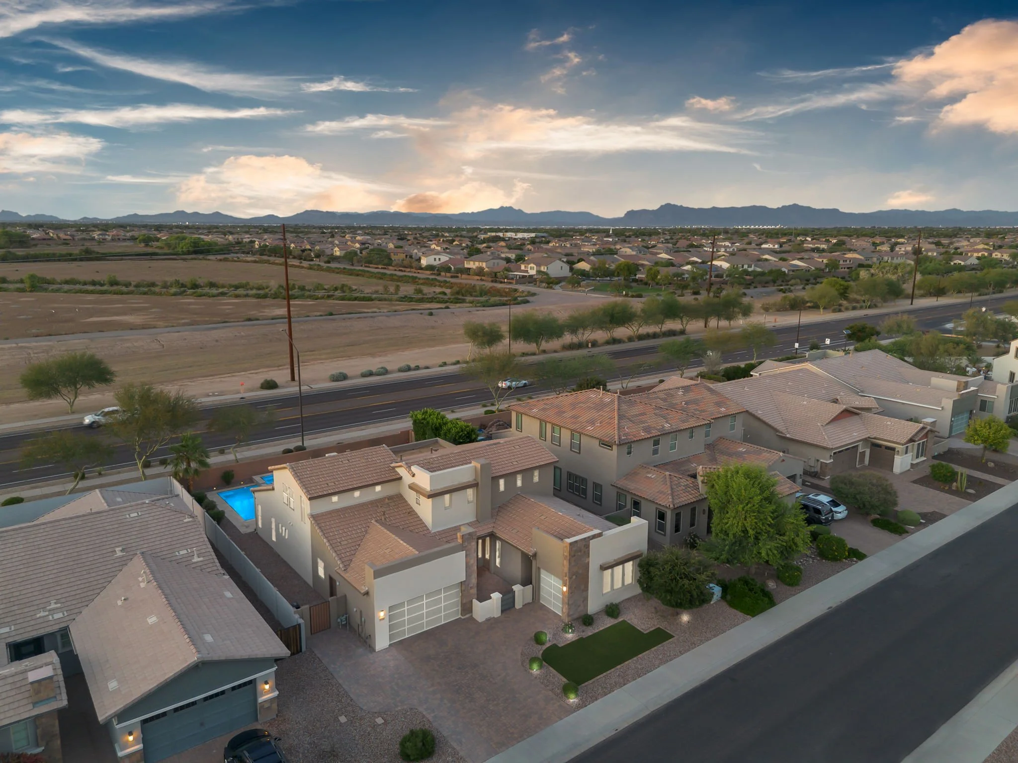 A suburban neighborhood with houses, a street, trees, and mountains in the background under a partly cloudy sky during the day.