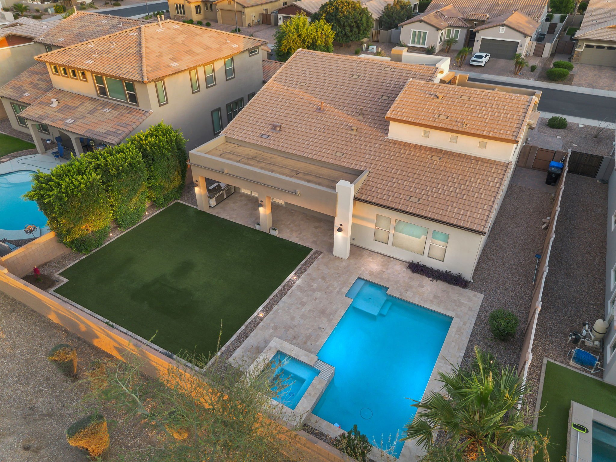 Aerial view of a residential backyard featuring a swimming pool, a grassy lawn, and surrounding houses with tiled roofs.