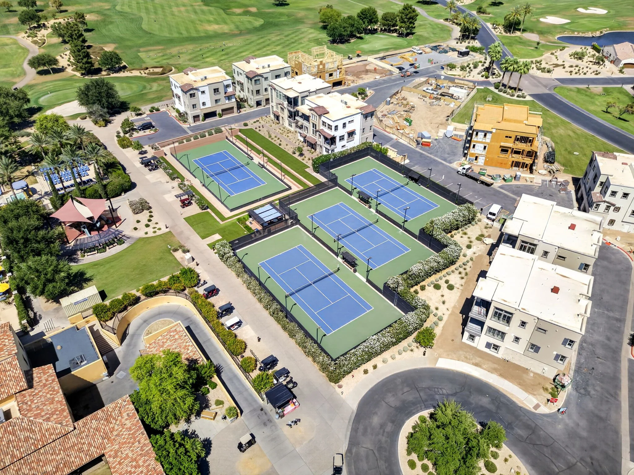 Aerial view of a community with tennis courts, construction site, golf course, and residential buildings.