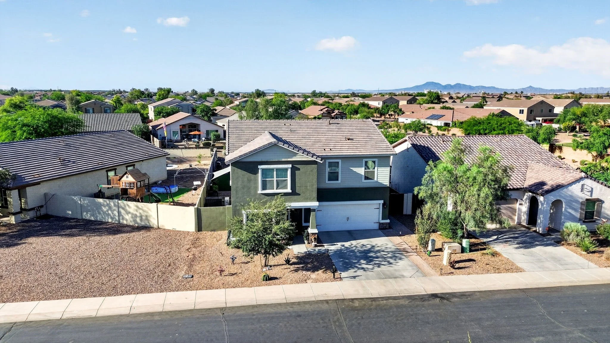 Aerial view of a suburban neighborhood with houses, trees, and mountains in the distance under a blue sky.
