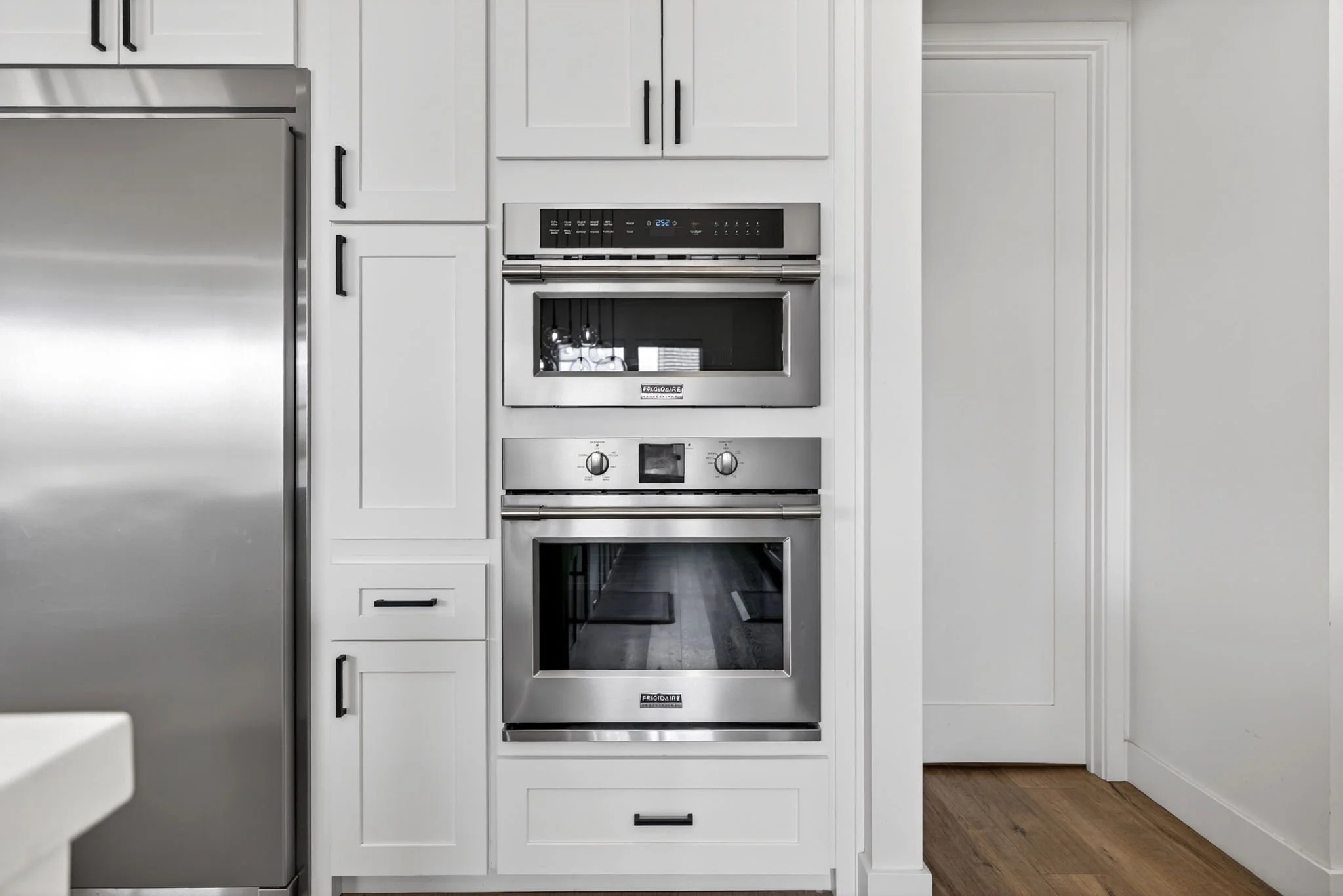 Modern kitchen with built-in stainless steel oven, black cabinet handles, and white cabinetry, with a hardwood floor.