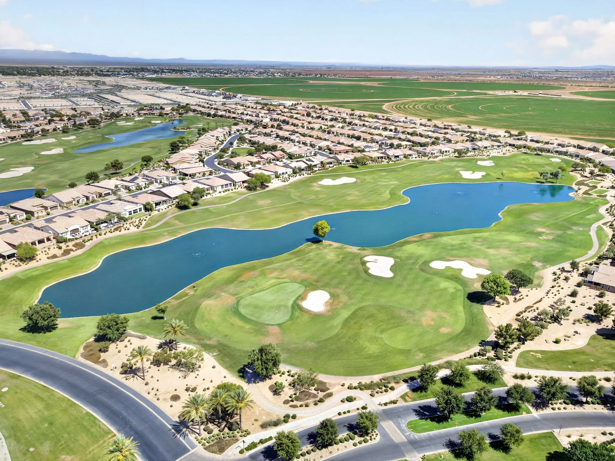 Aerial view of a golf course with lakes, surrounded by residential houses and a suburban area in the background.