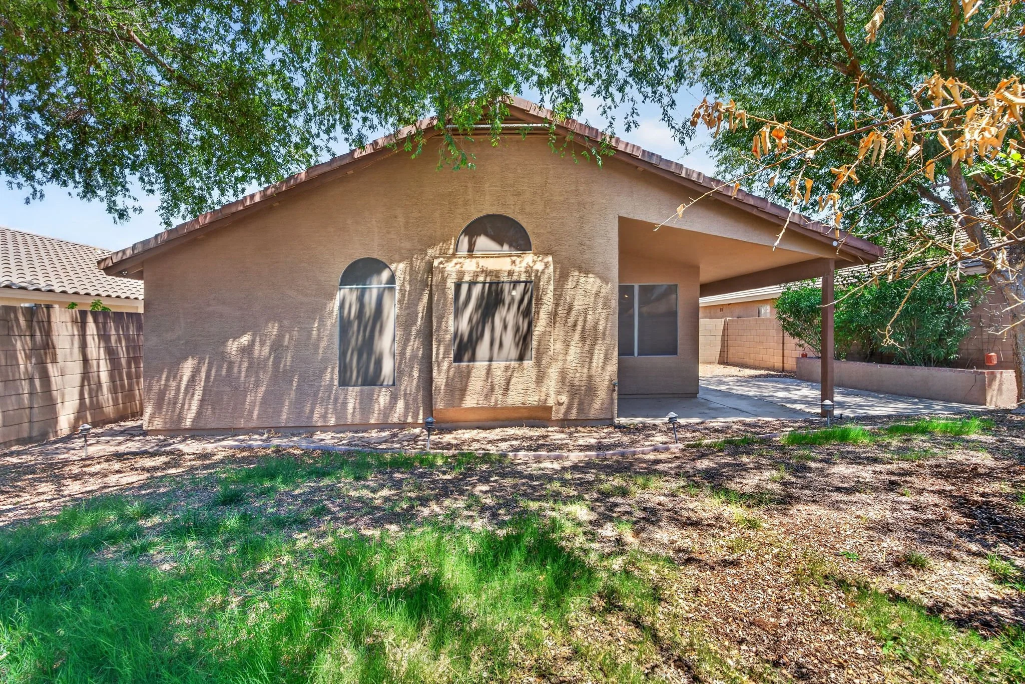 Backyard view of a house with beige stucco walls, a tiled roof, and surrounded by trees and a wooden fence.