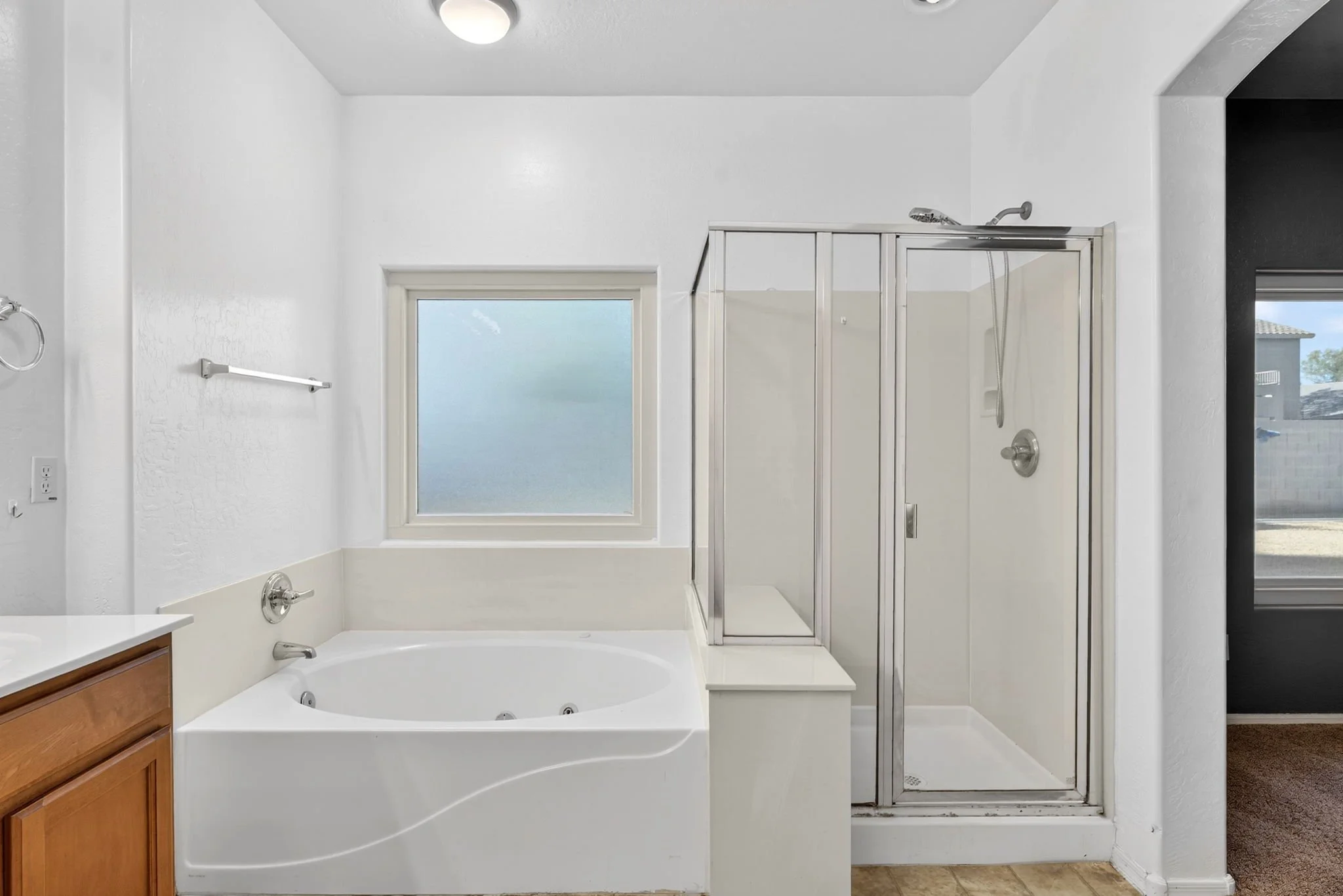 A bathroom with a bathtub, a window, a shower enclosure, and a dark-colored wall on the right.