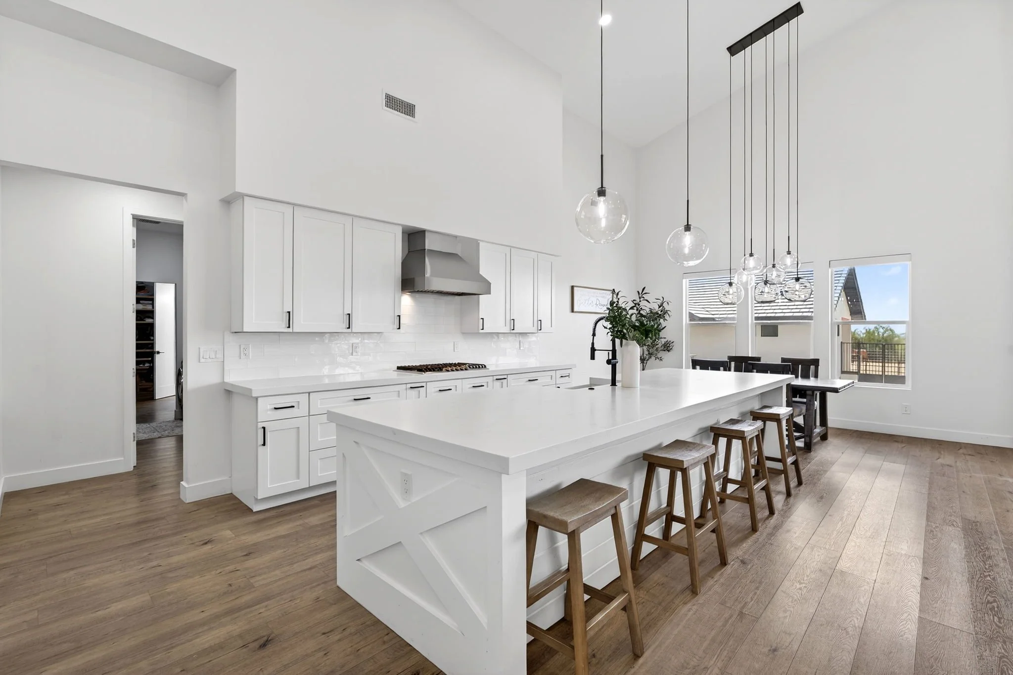Modern kitchen with white cabinets, a large island, and pendant lights over the island, with wooden stools and large windows