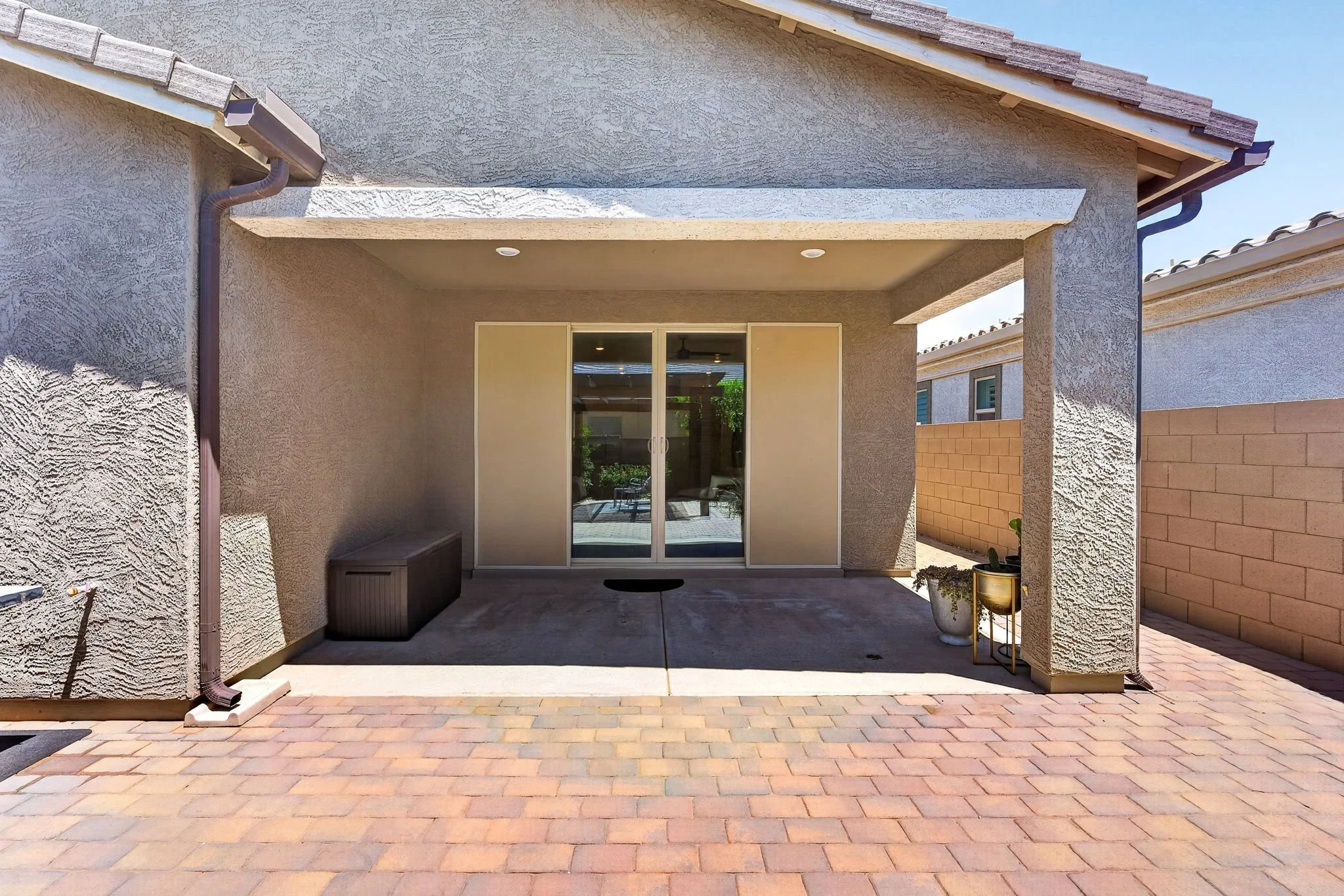View of a suburban house backyard with a sliding glass door, covered patio, brick paving, and decorative potted plants.