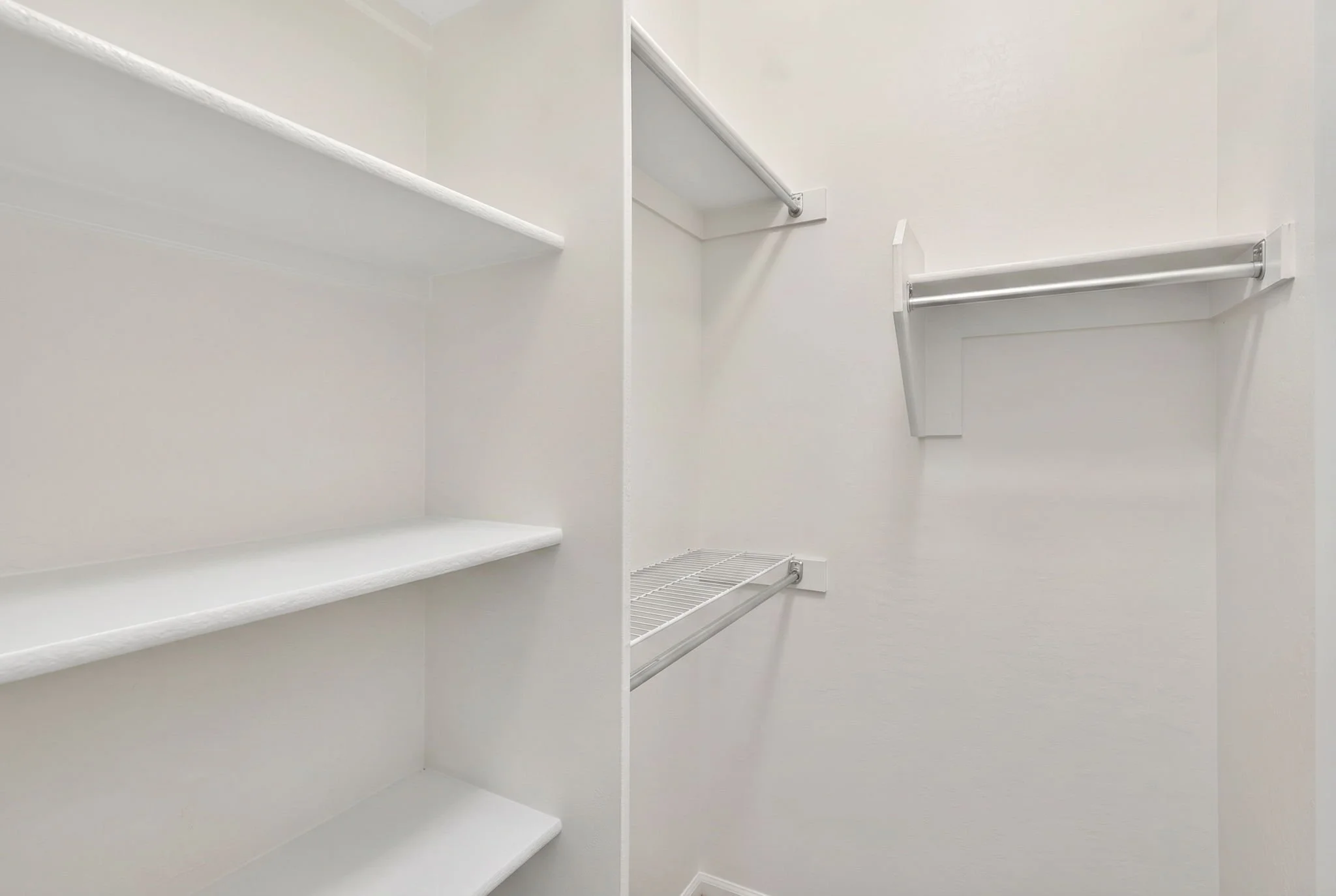 Empty white walk-in closet with shelves and clothing rods.