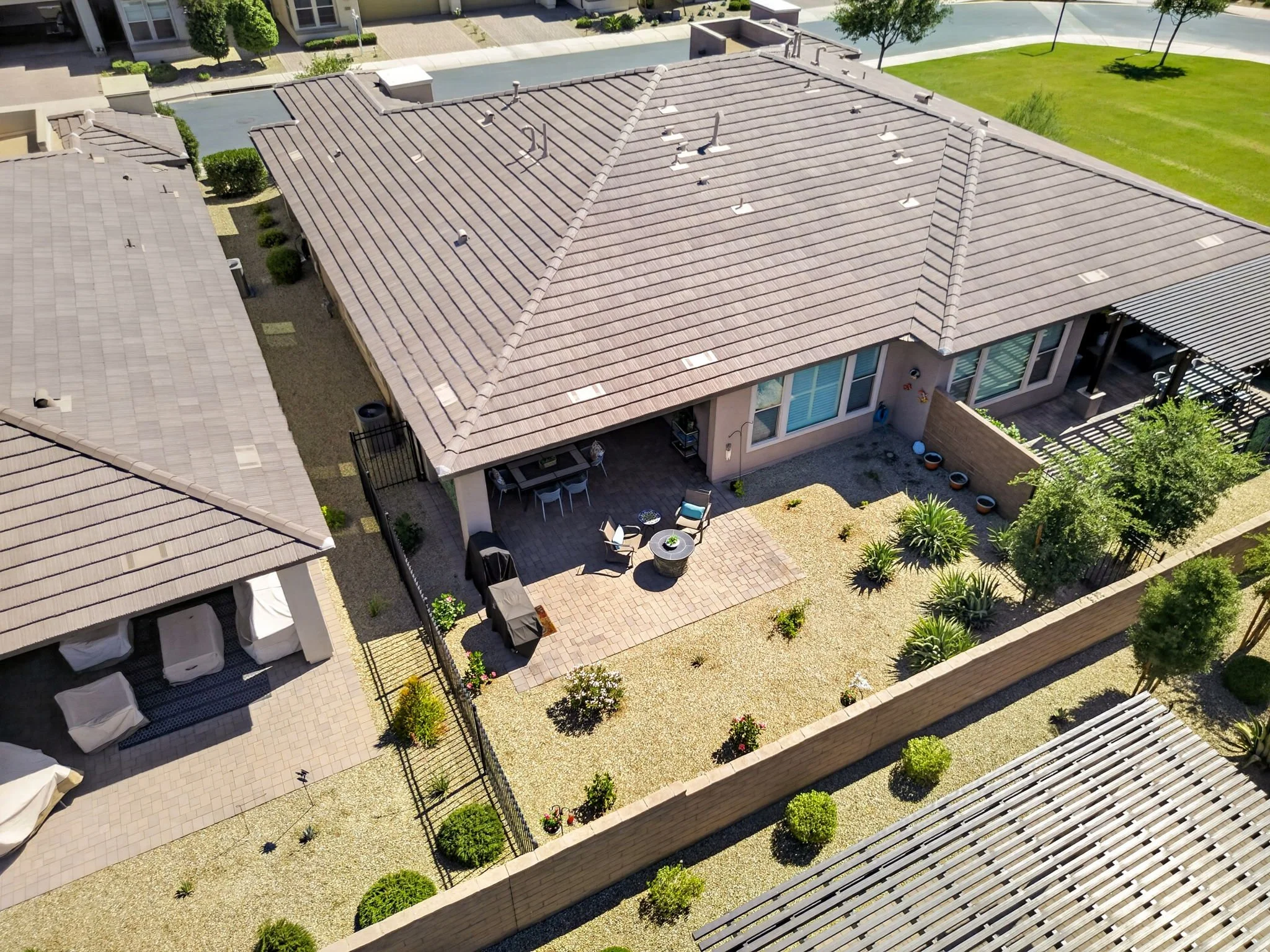 Aerial view of a residential backyard with a patio, outdoor furniture, landscaped garden, and neighboring houses.