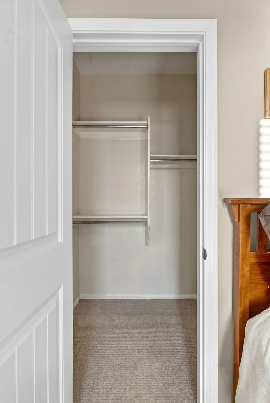 Empty closet with white shelves and rods, beige carpet, and white trim.