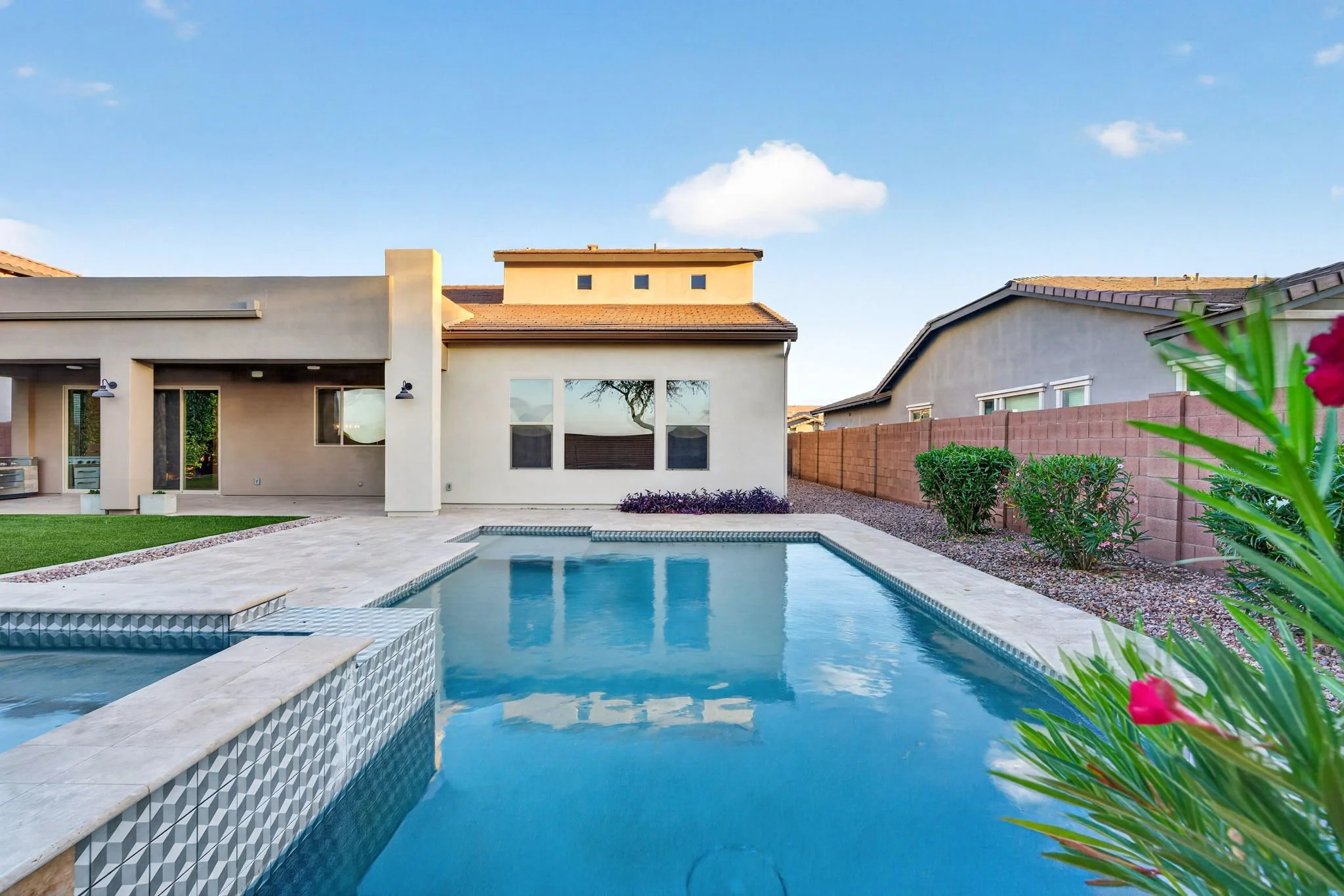 Backyard with swimming pool, patio, and modern house under blue sky with a few clouds.