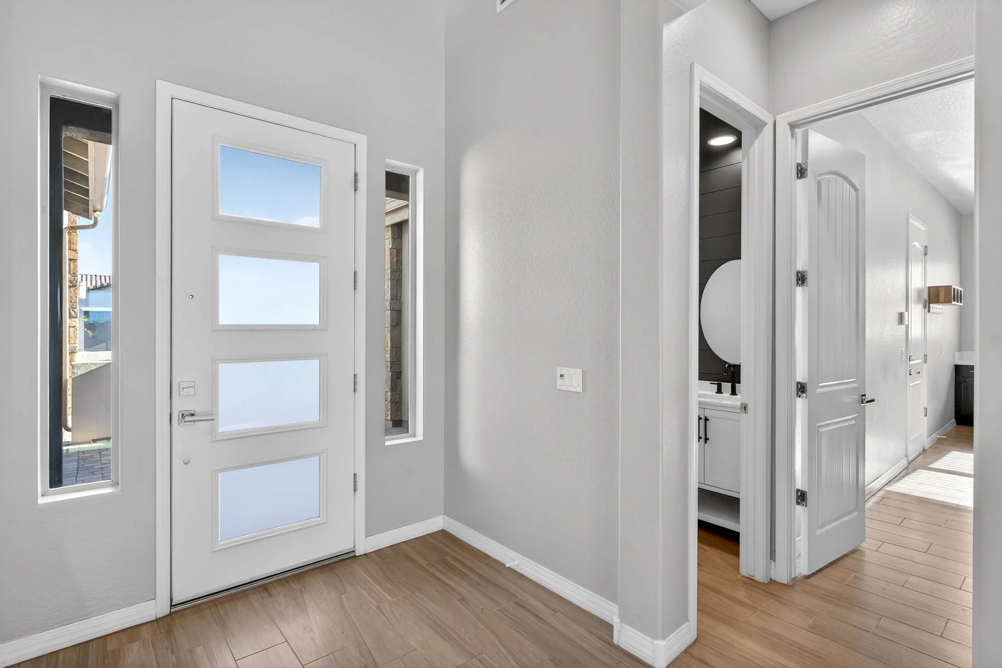 Interior entryway with white front door, wooden flooring, and a hallway with a black and white color scheme and visible cabinetry.
