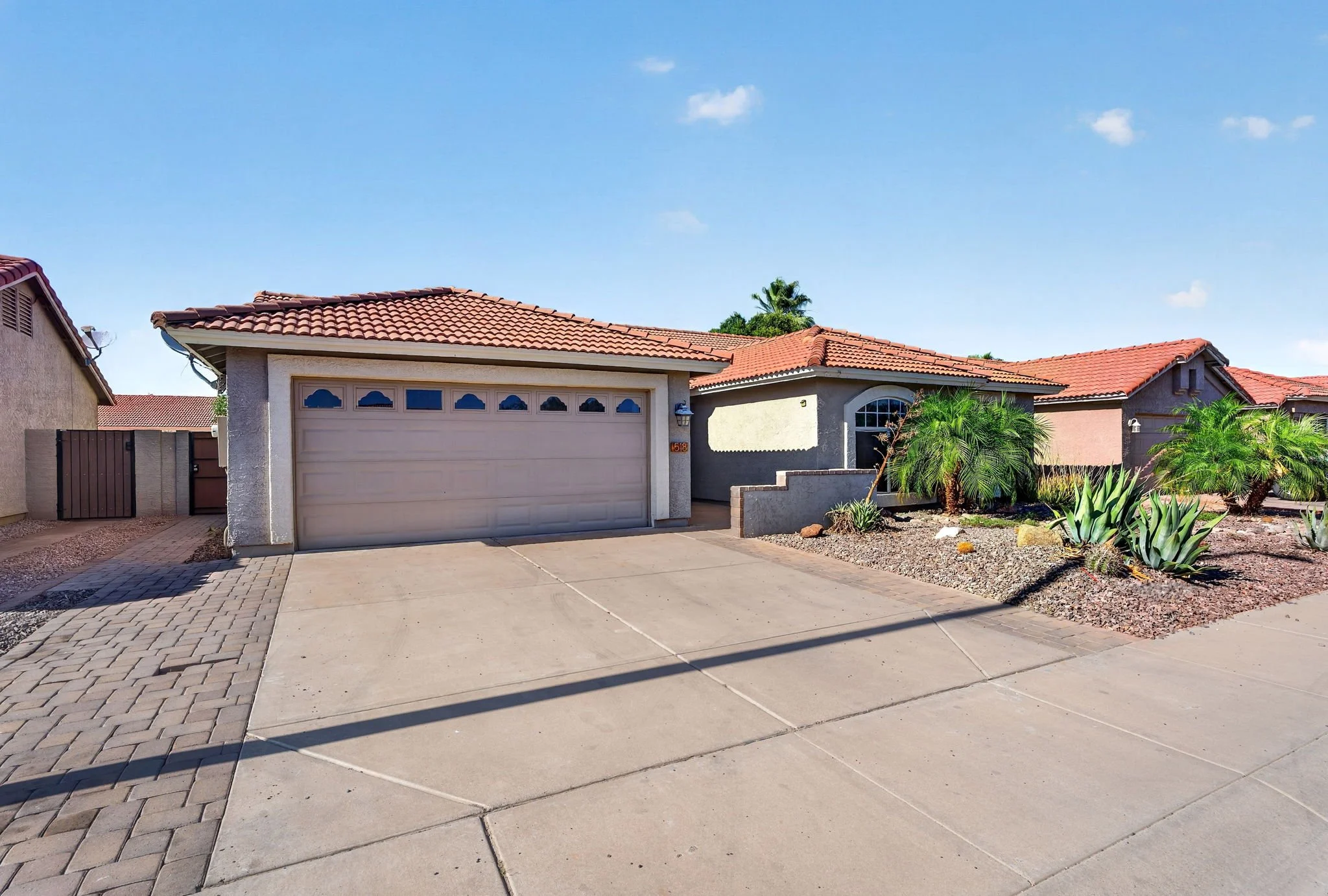 Front of a house with a closed garage door, a driveway, desert landscaping, and a clear blue sky.