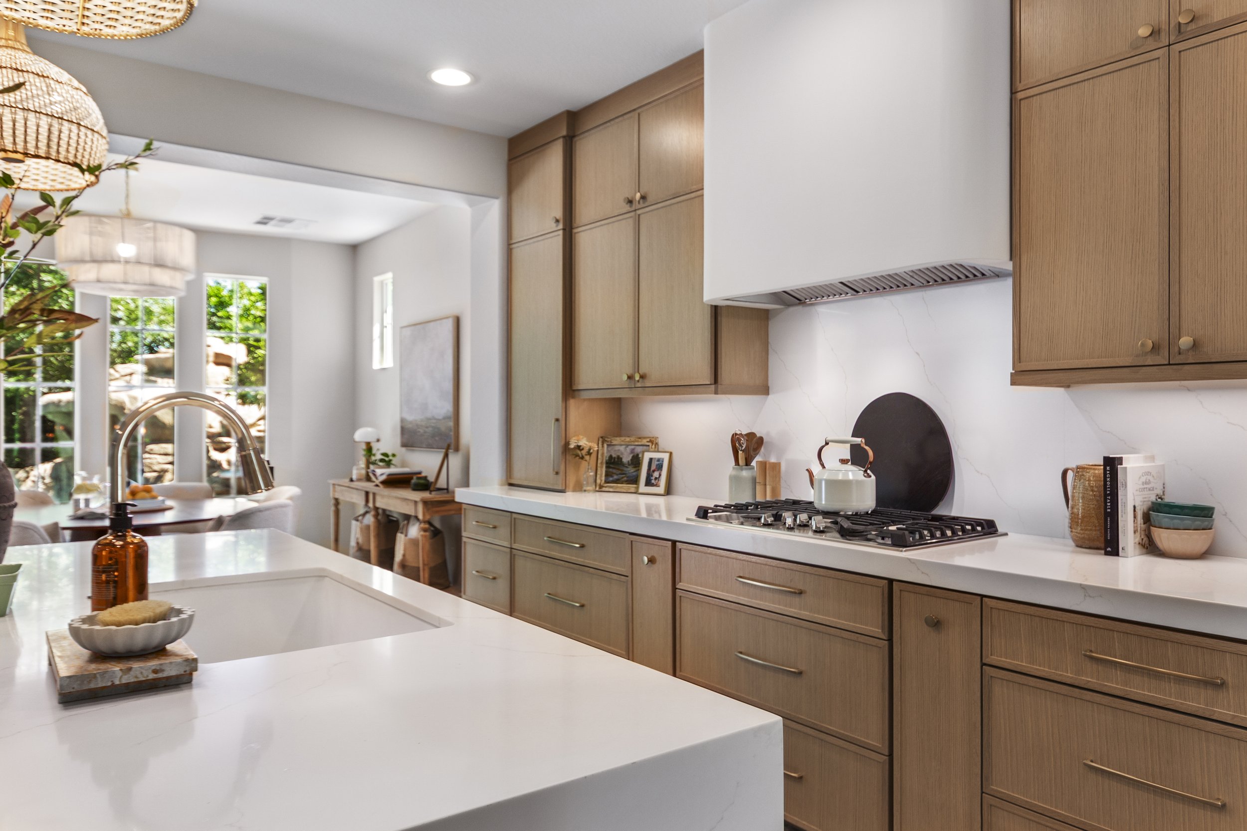 Modern kitchen with light wood cabinets, white countertops, a gas stove, and natural light from large windows.