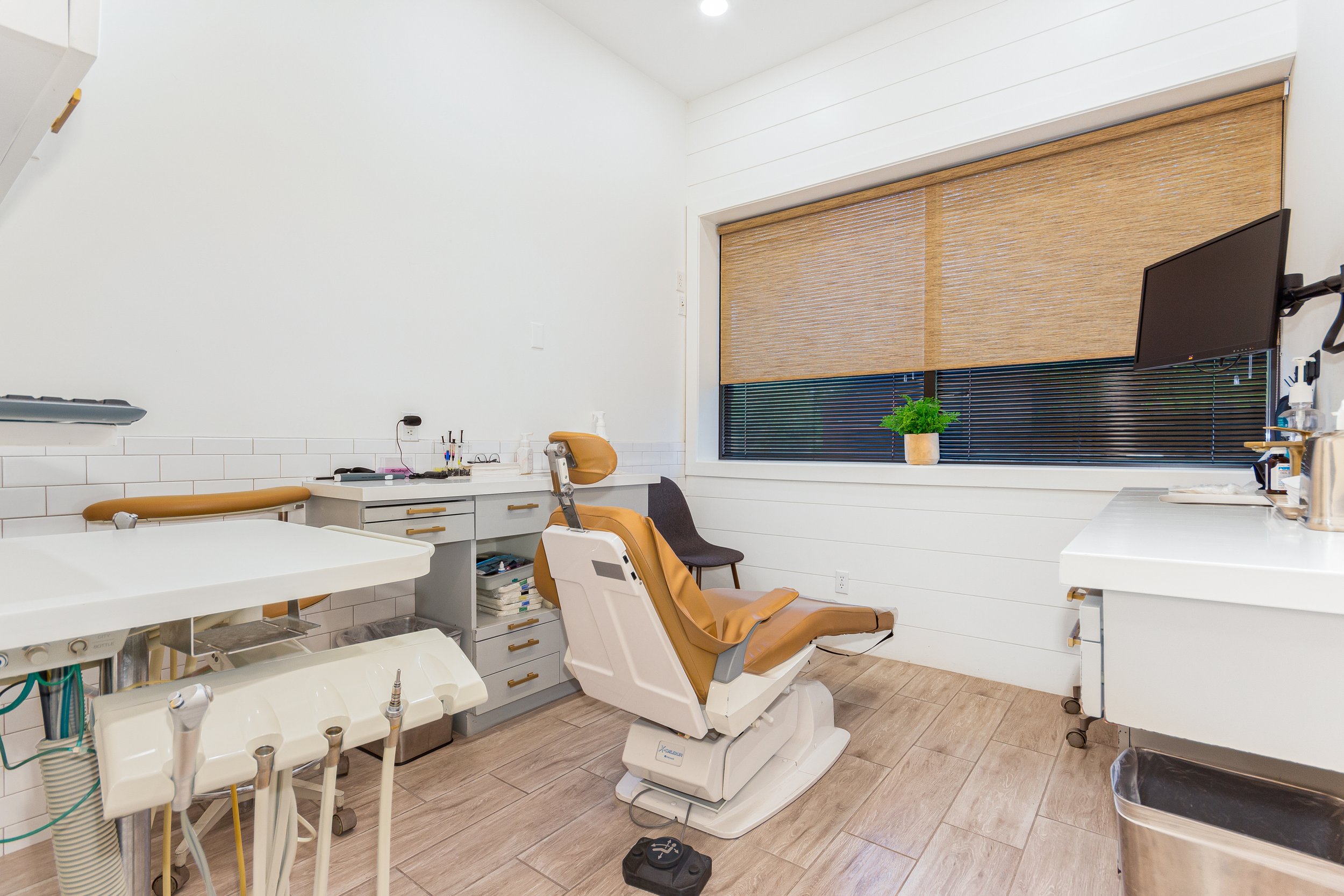 A dental office treatment room with dental chair, dental equipment, and a monitor on the wall.