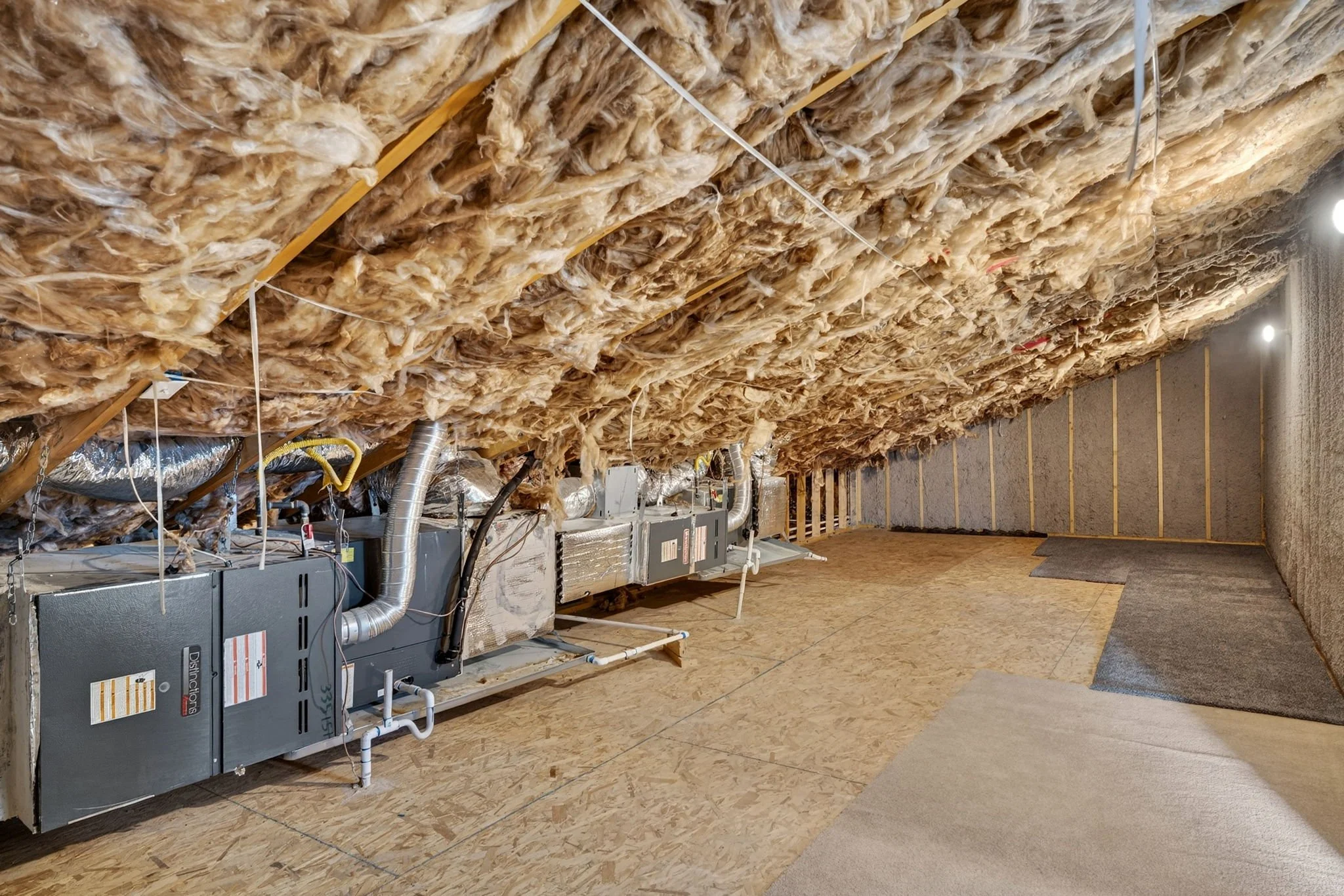 An unfinished basement with new insulation on the ceiling, HVAC system, ductwork, and a gray carpet on the floor.