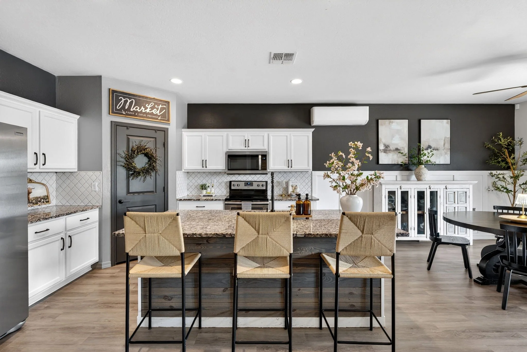 Modern kitchen with white cabinets, black accents, granite island, stainless steel appliances, and dining area with beige chairs and a round table.