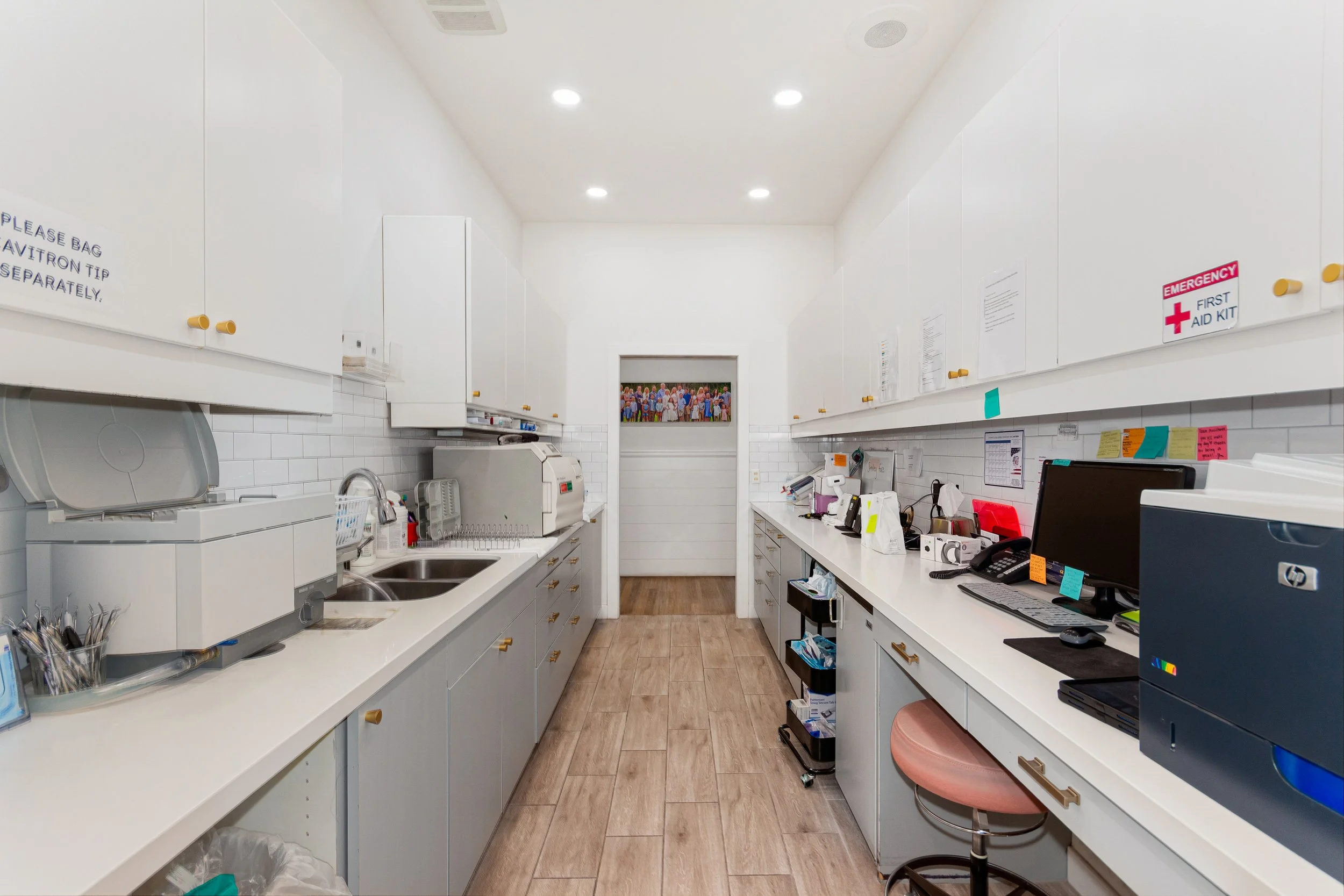 A clean, organized hospital or medical clinic reception or work area with white cabinets, countertop, and medical equipment, featuring a door at the back with a colorful photo of a group of people.