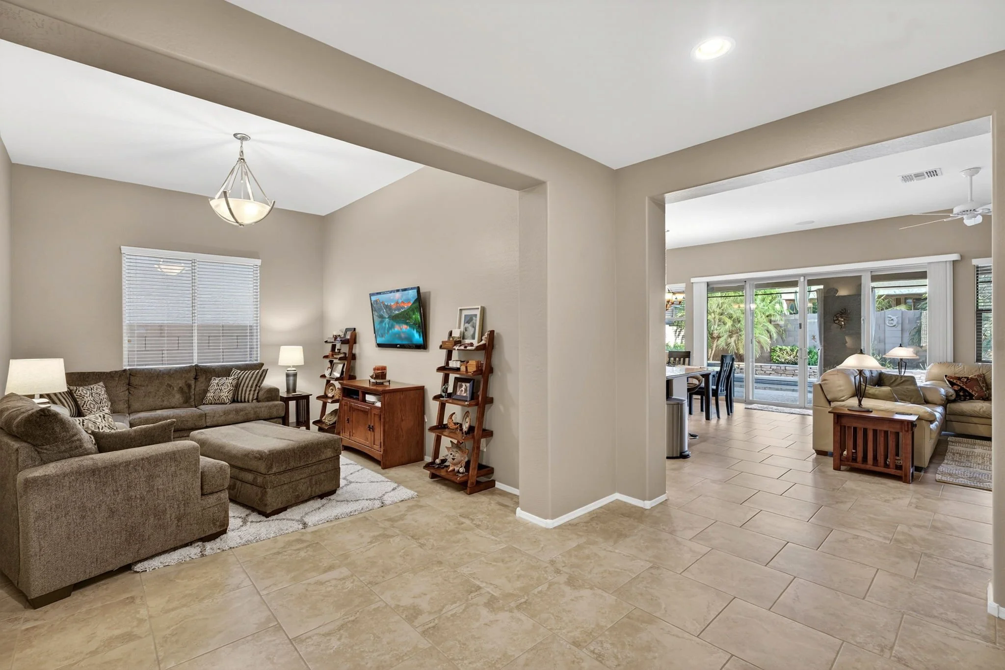 Open-concept living room and dining area with beige tile flooring, beige walls, and large windows allowing natural light.