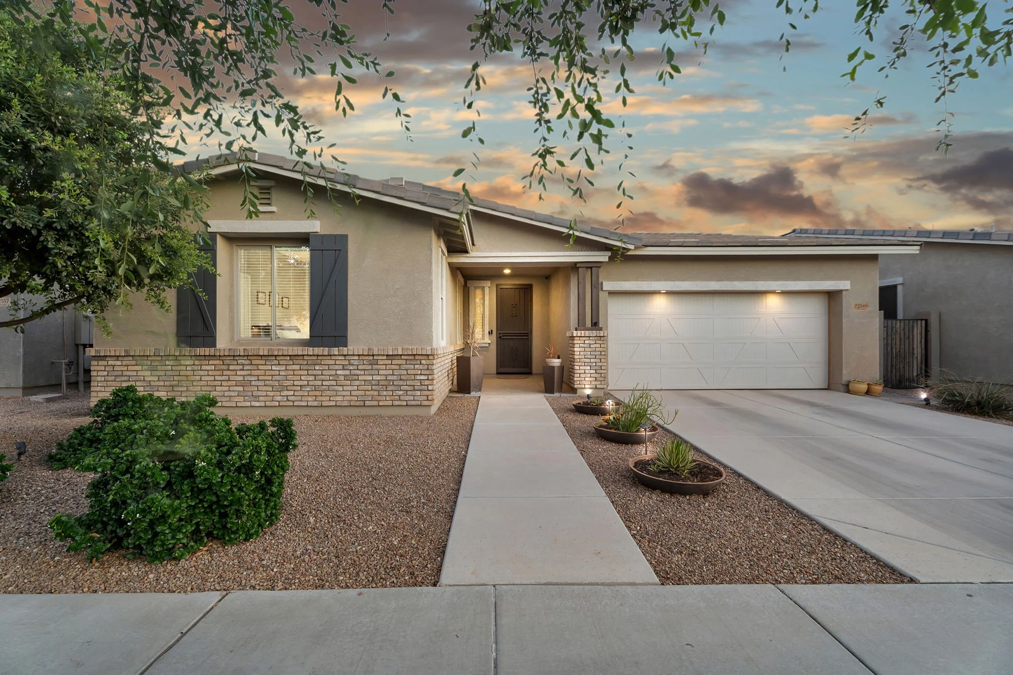 Front view of a suburban house at sunset with a driveway, plants, and trees.